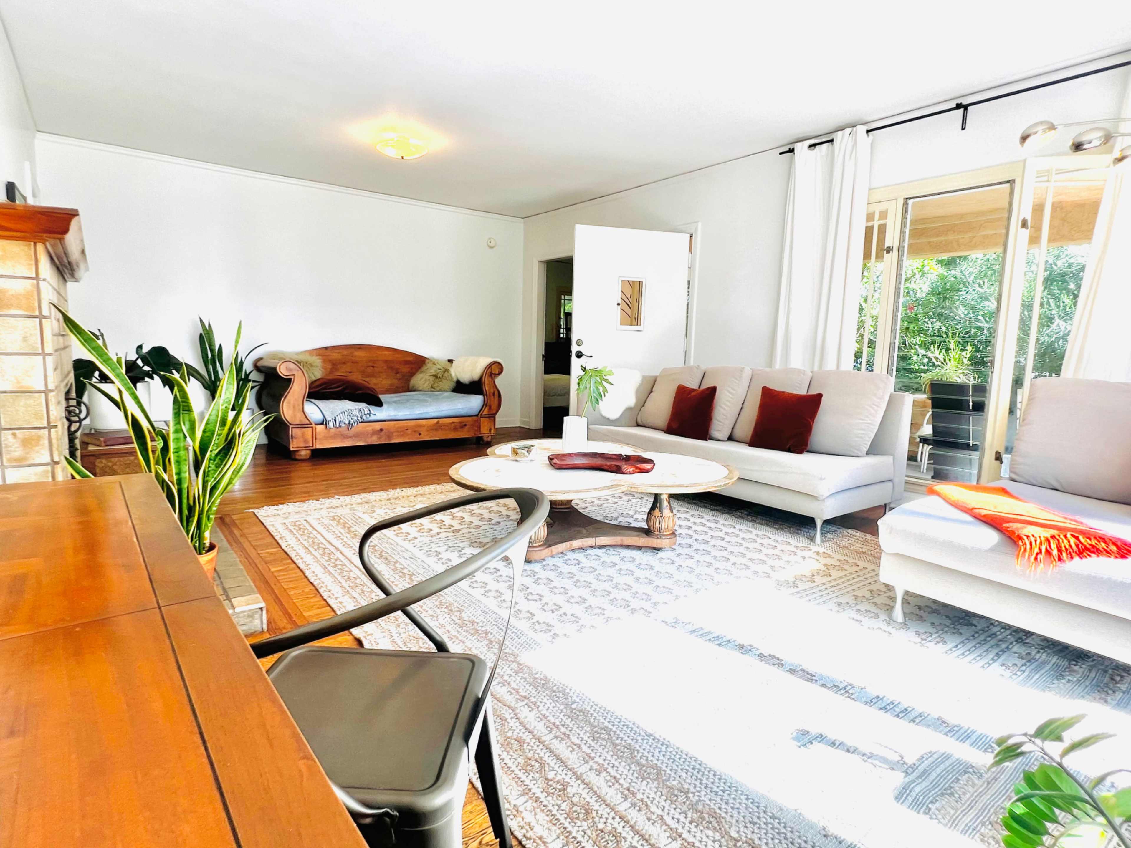 The room features a furnished living space with a wooden desk, two sofas, a circular coffee table, and large windows allowing natural light.