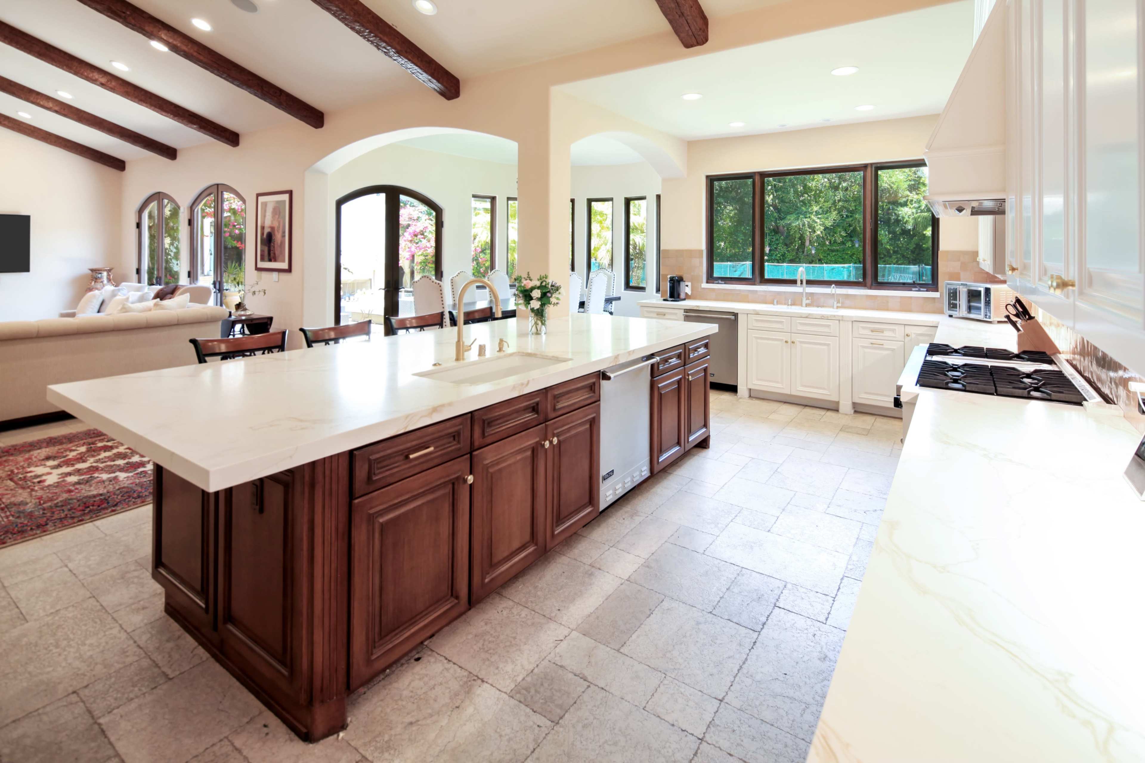 A spacious kitchen with a large central island, wooden cabinetry, and a view of an outdoor area through large windows.