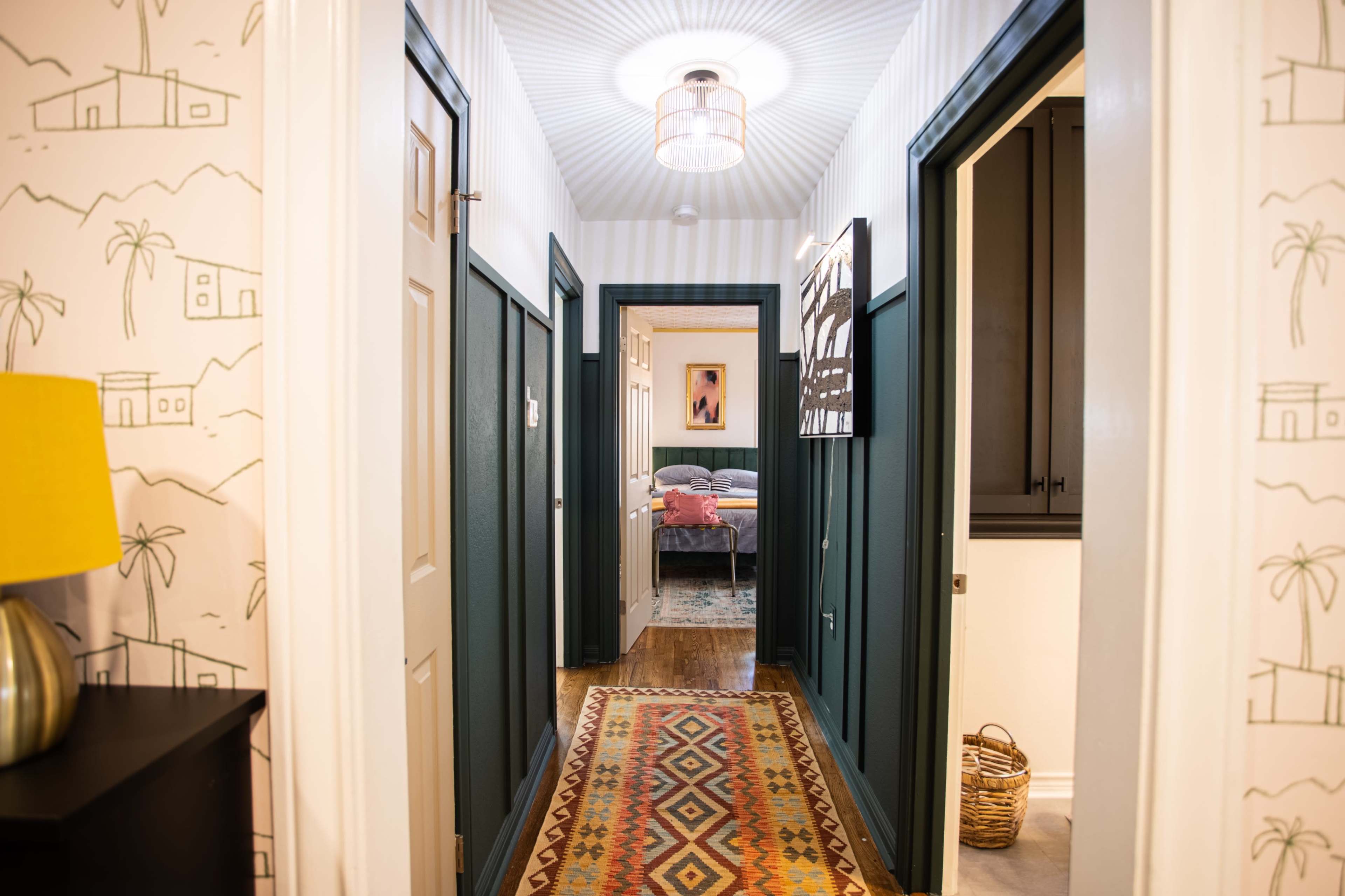 A well-lit hallway with green paneled walls, a patterned runner rug, and doors on either side leading to rooms.
