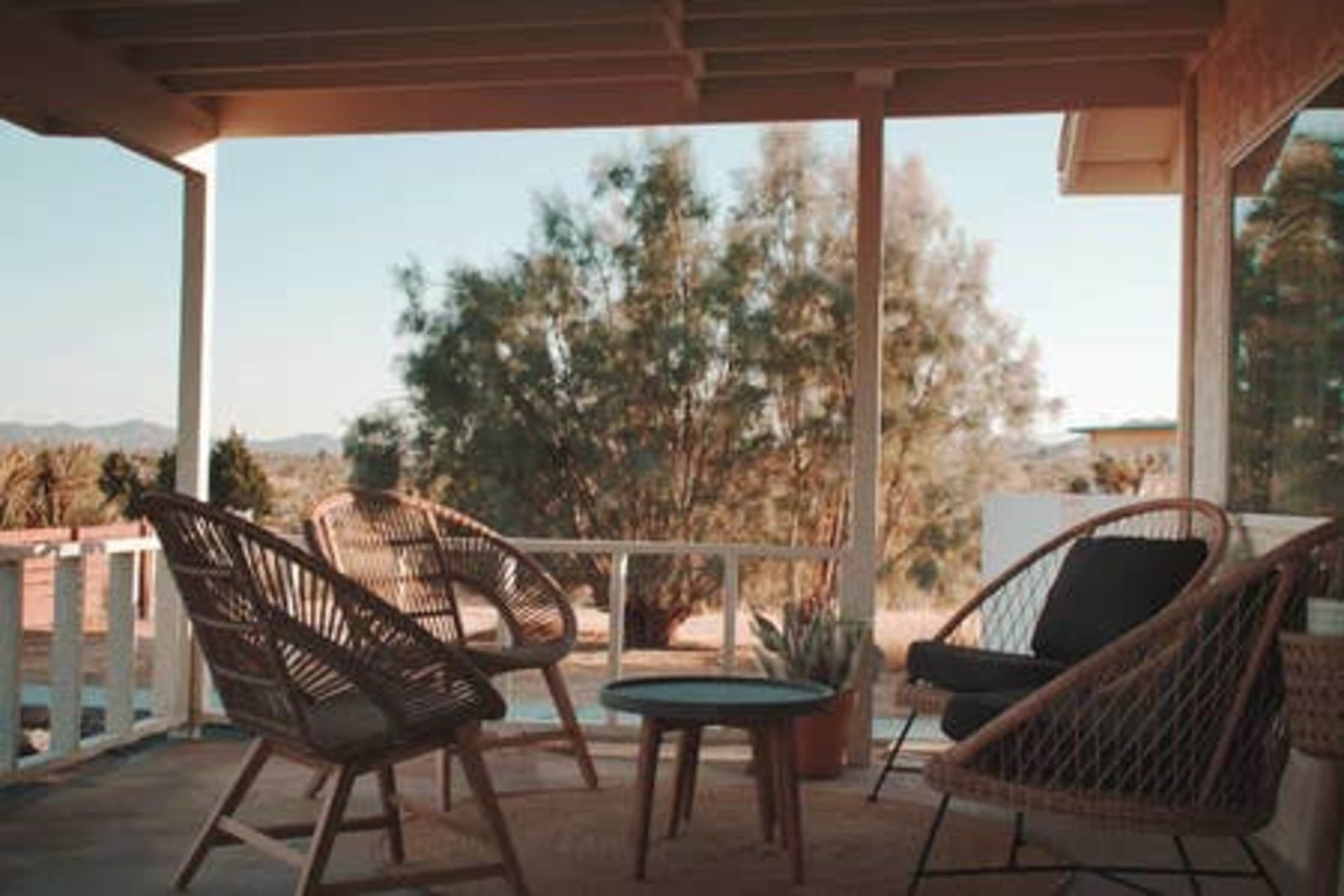 A porch features two rattan chairs and a small table surrounded by desert vegetation.