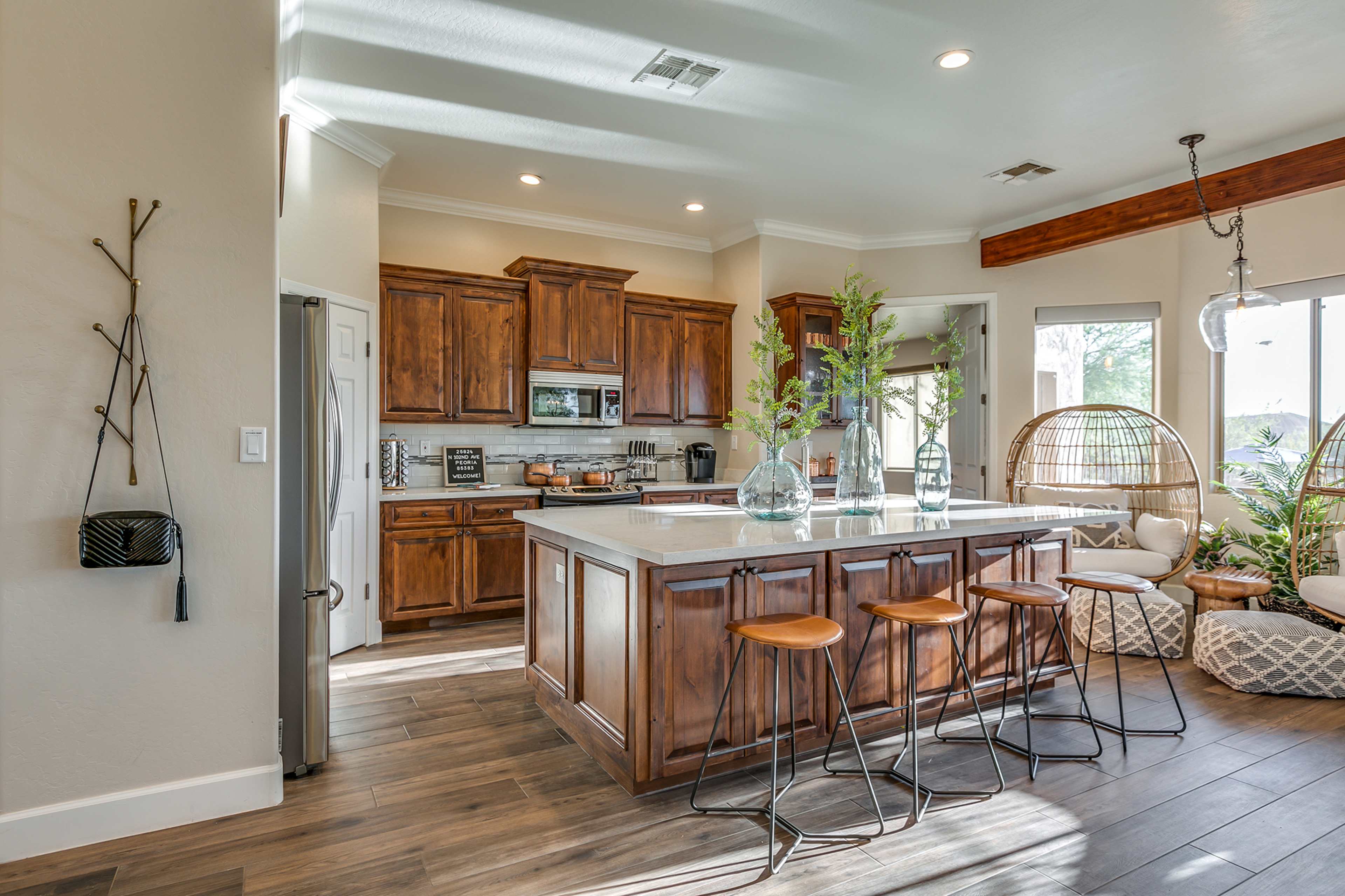 A modern kitchen with wooden cabinets, white countertops, and a central island with four bar stools.