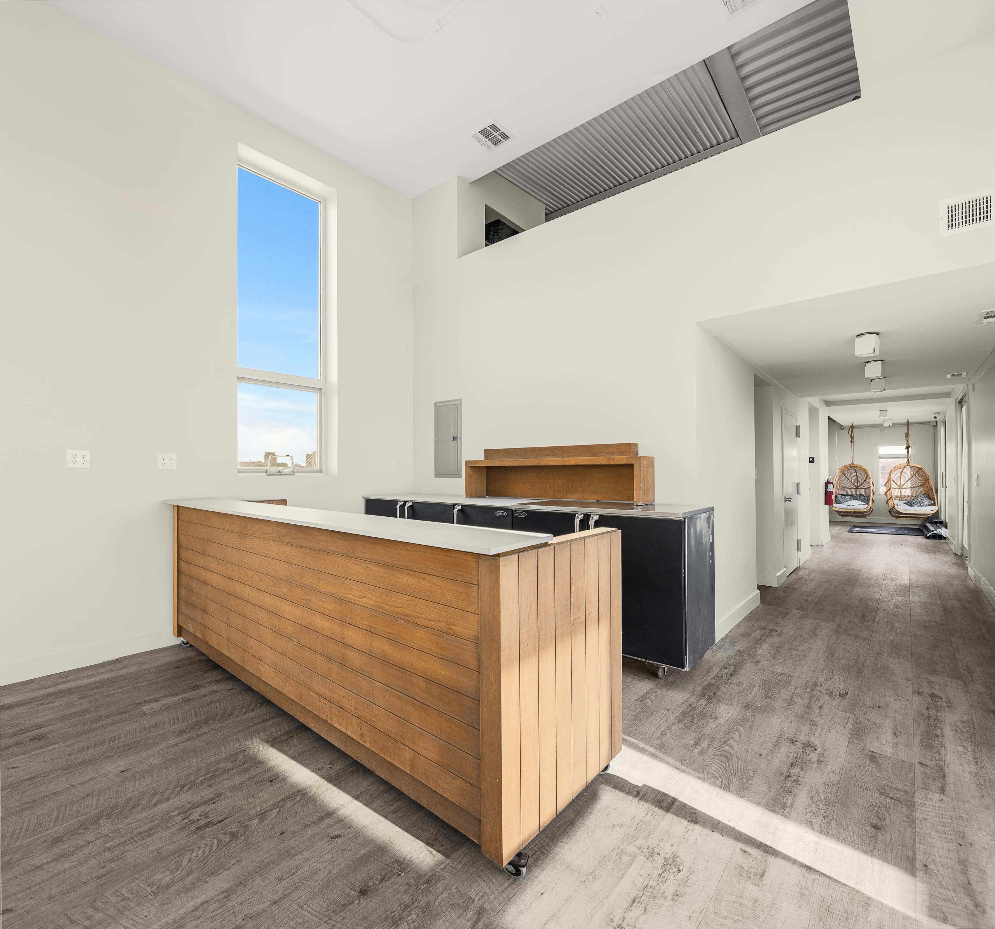 The image features a spacious interior with a wooden reception desk on the left and a hallway leading to rooms on the right.