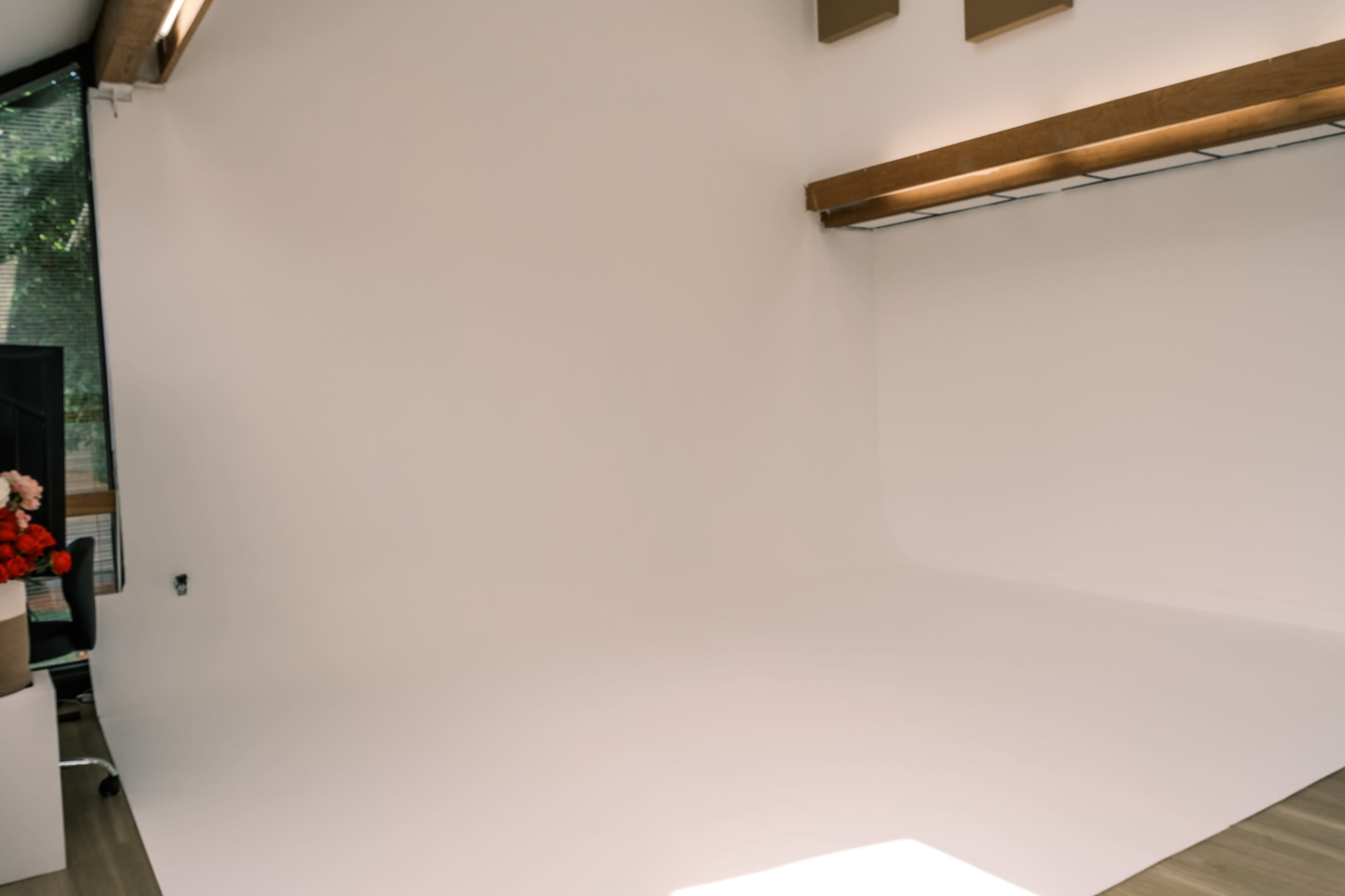 The image shows a minimalistic room with a white backdrop, a wooden beam, and a shelf, featuring a few decorative items in the corner.