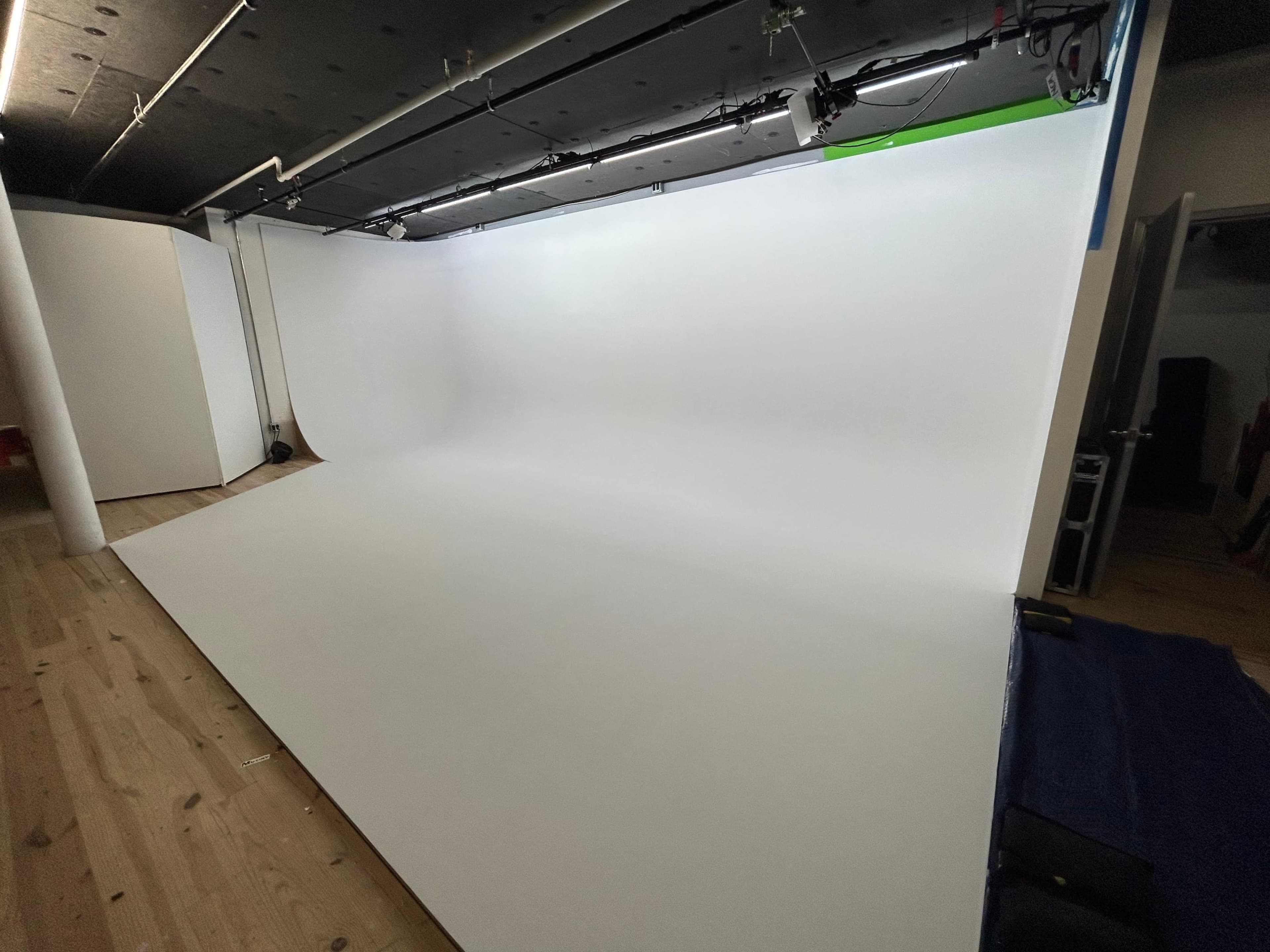 The image shows a spacious photography studio with a white backdrop and wooden flooring.