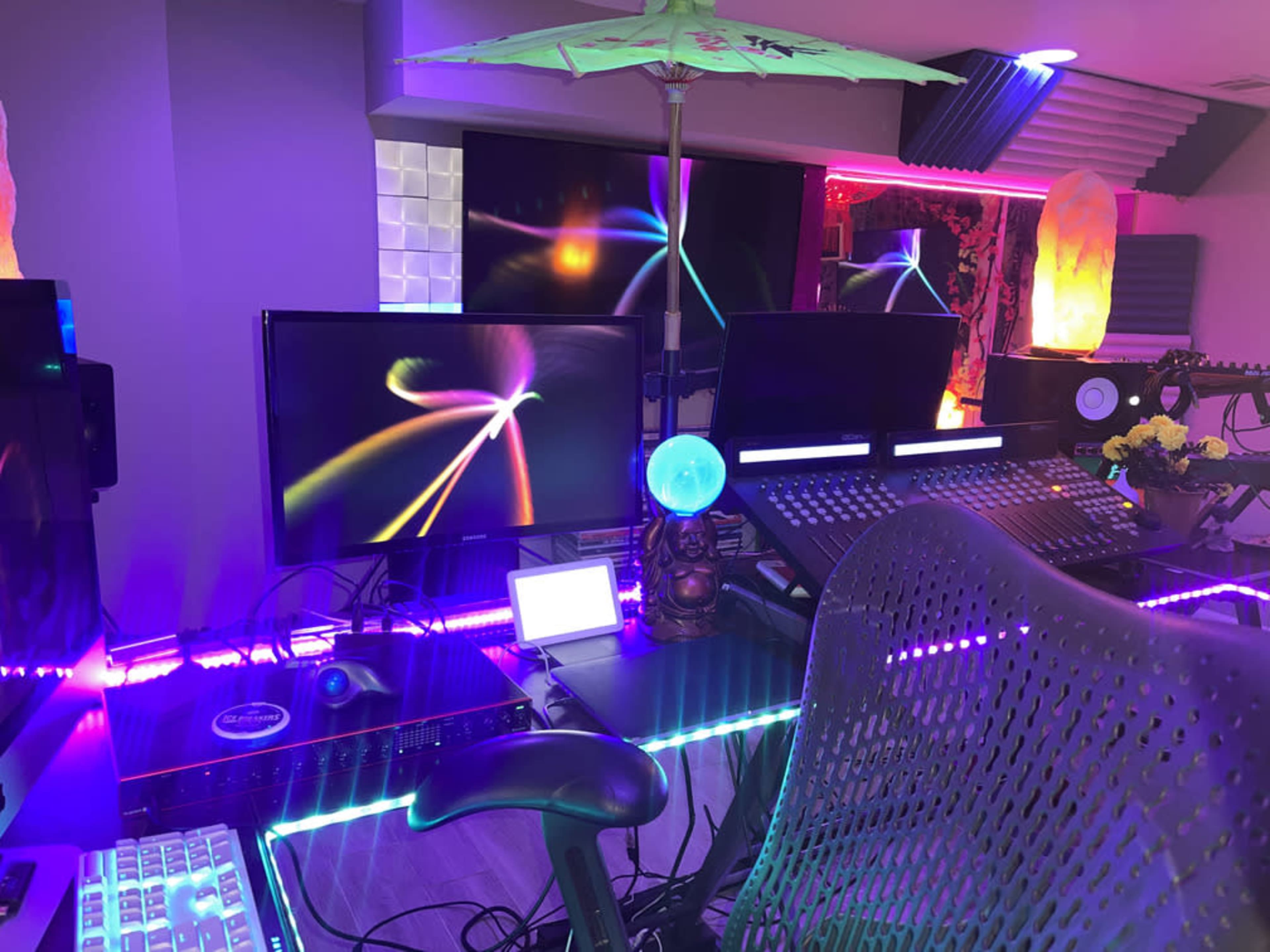 A modern music production studio featuring multiple monitors, a colorful lighting setup, and a decorative umbrella.