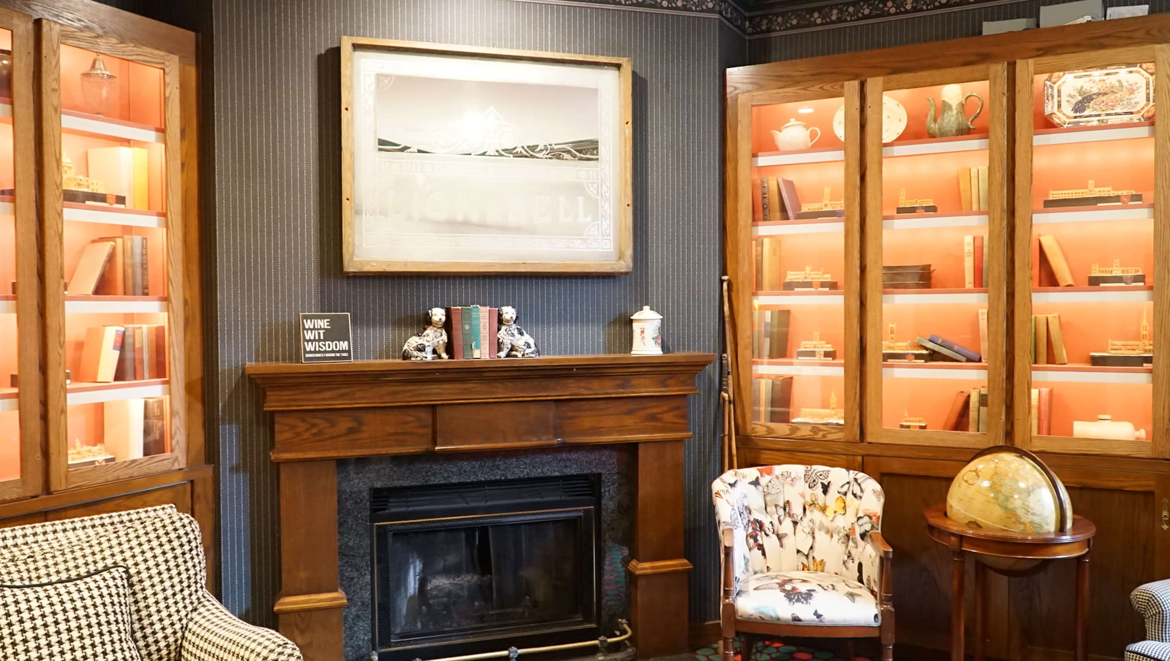 A cozy room with a fireplace surrounded by wooden bookshelves and a patterned chair.