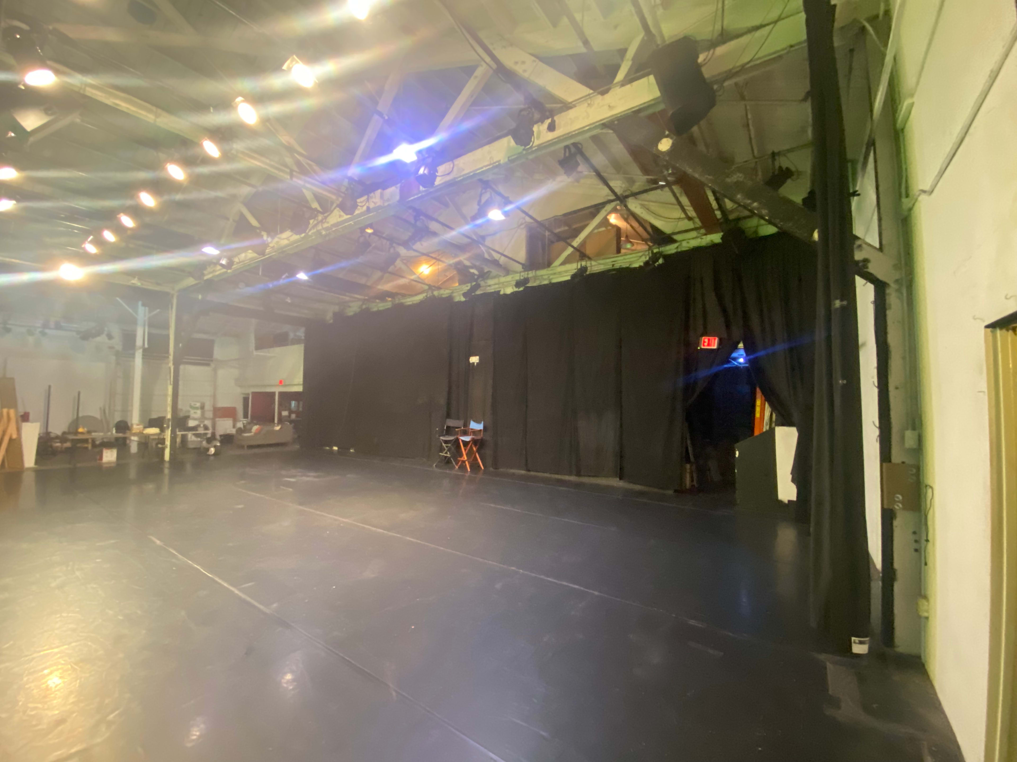 The image shows a spacious theater stage with a black curtain backdrop and dim lighting.