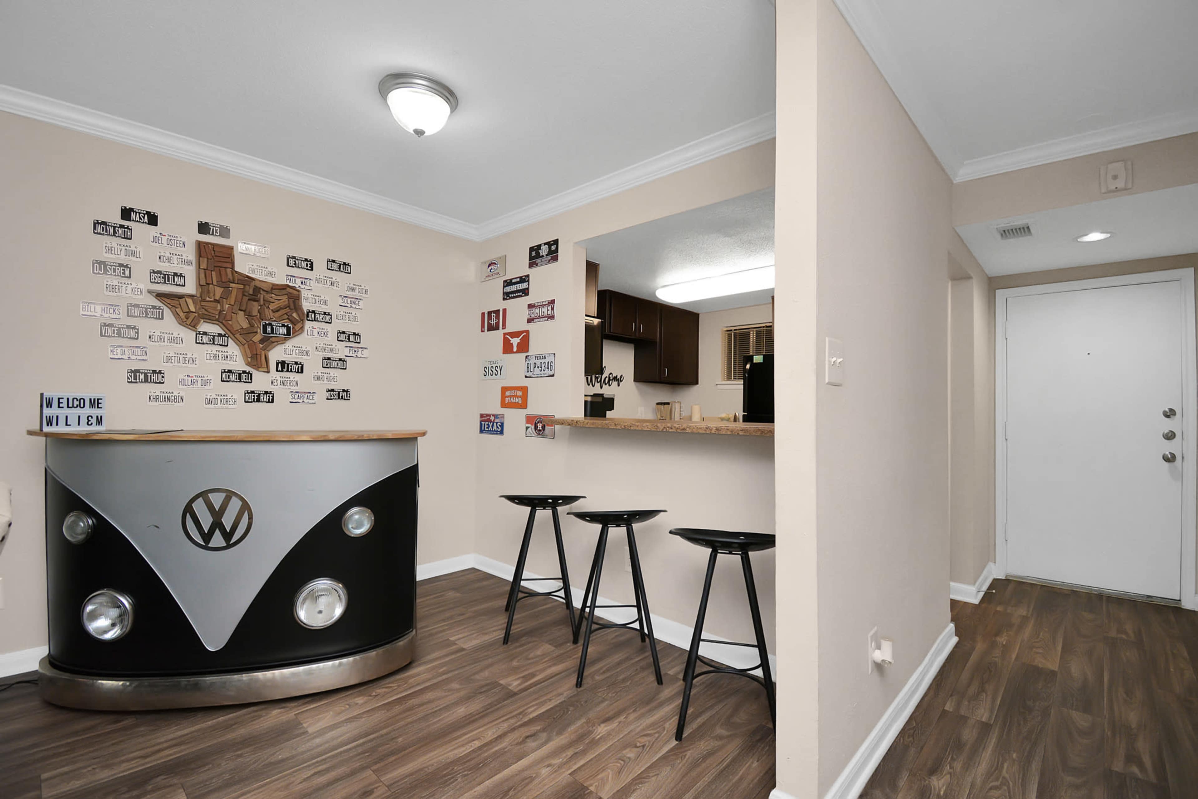 A modern entryway with a Volkswagen-themed bar counter and three black stools, leading to a kitchen area.