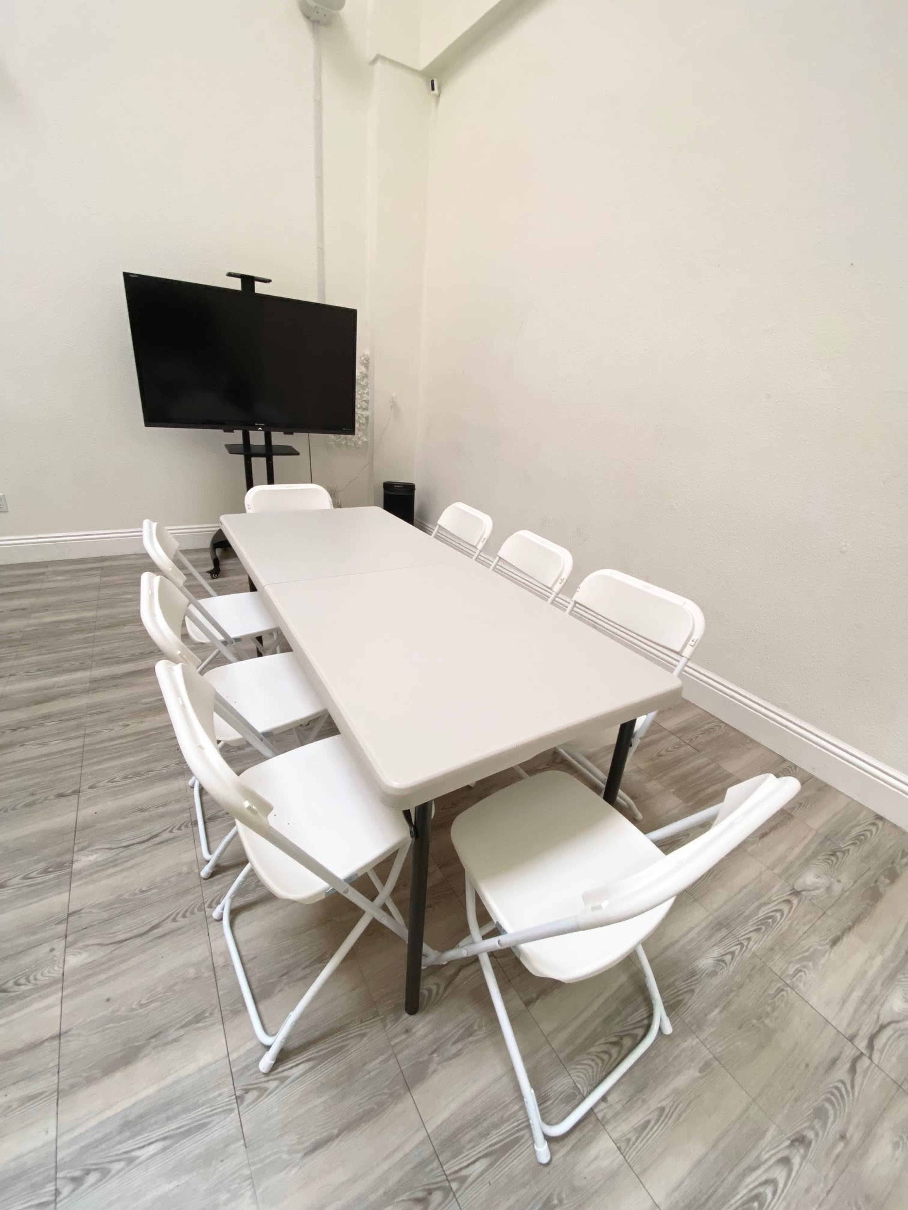 A rectangular table with six folding chairs is positioned in a room with a large television mounted on the wall.