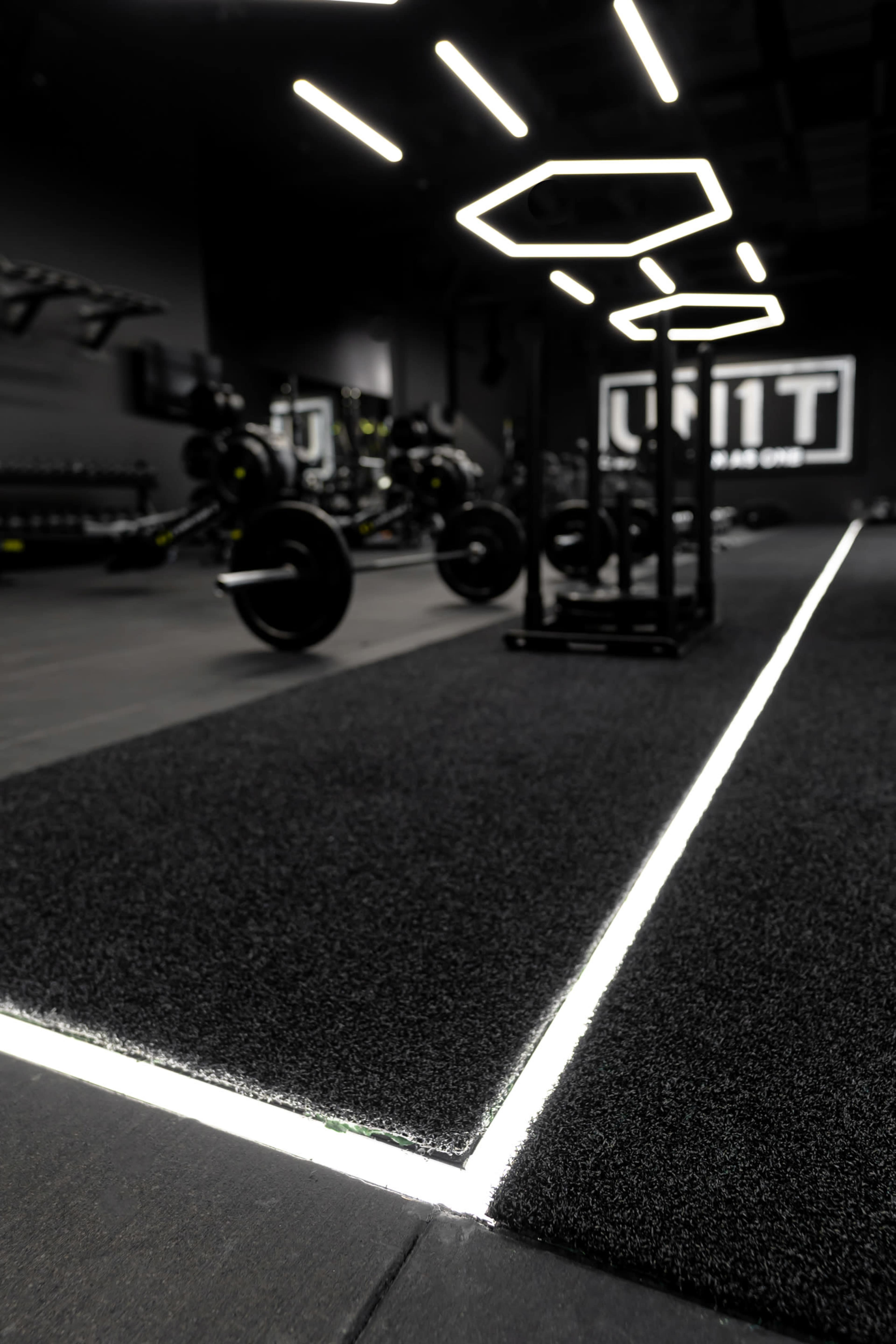 A modern gym interior featuring black flooring and illuminated geometric light fixtures above.