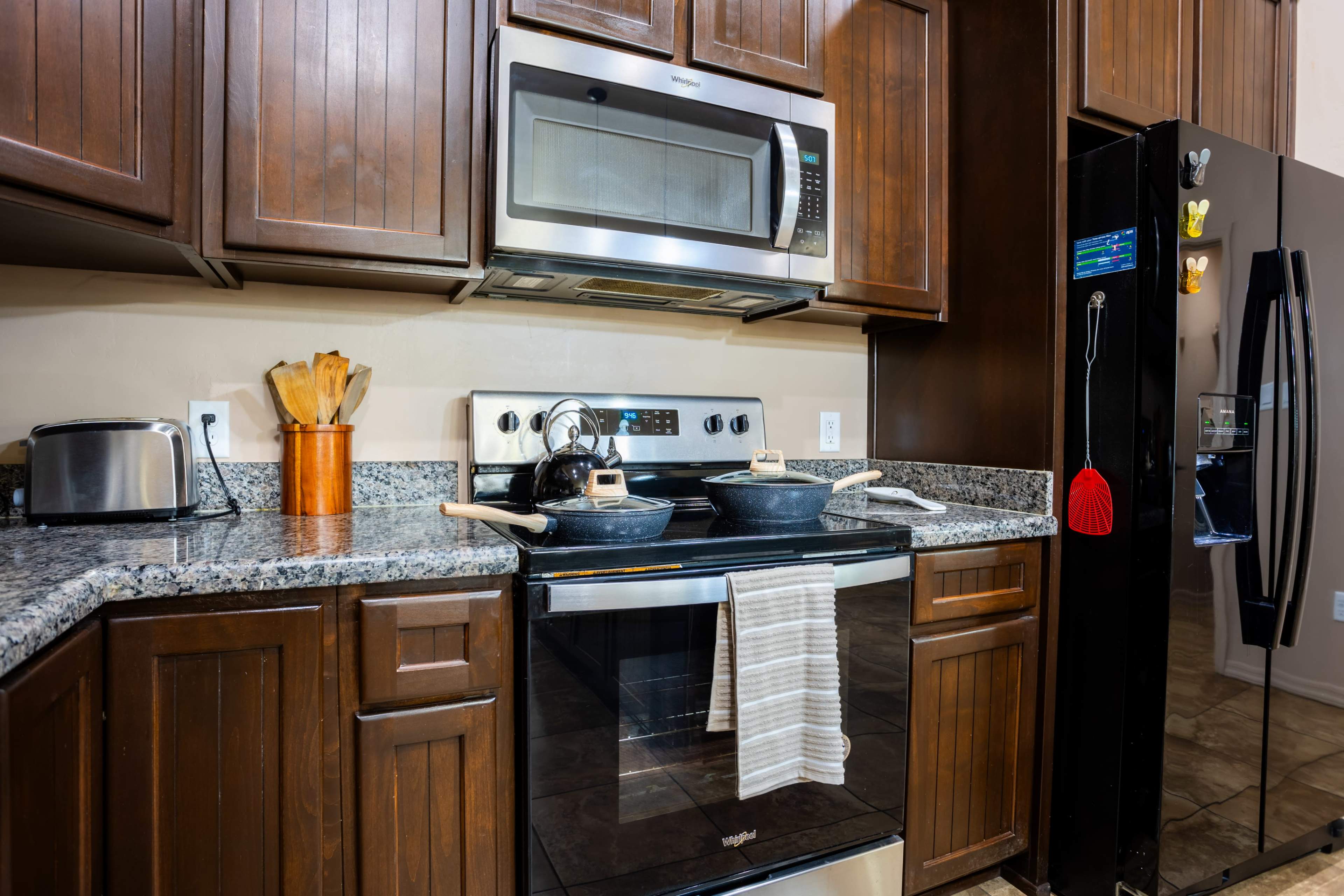 A kitchen with dark wood cabinets, a stainless steel microwave above a black stove, and two cast iron pans on the burners.