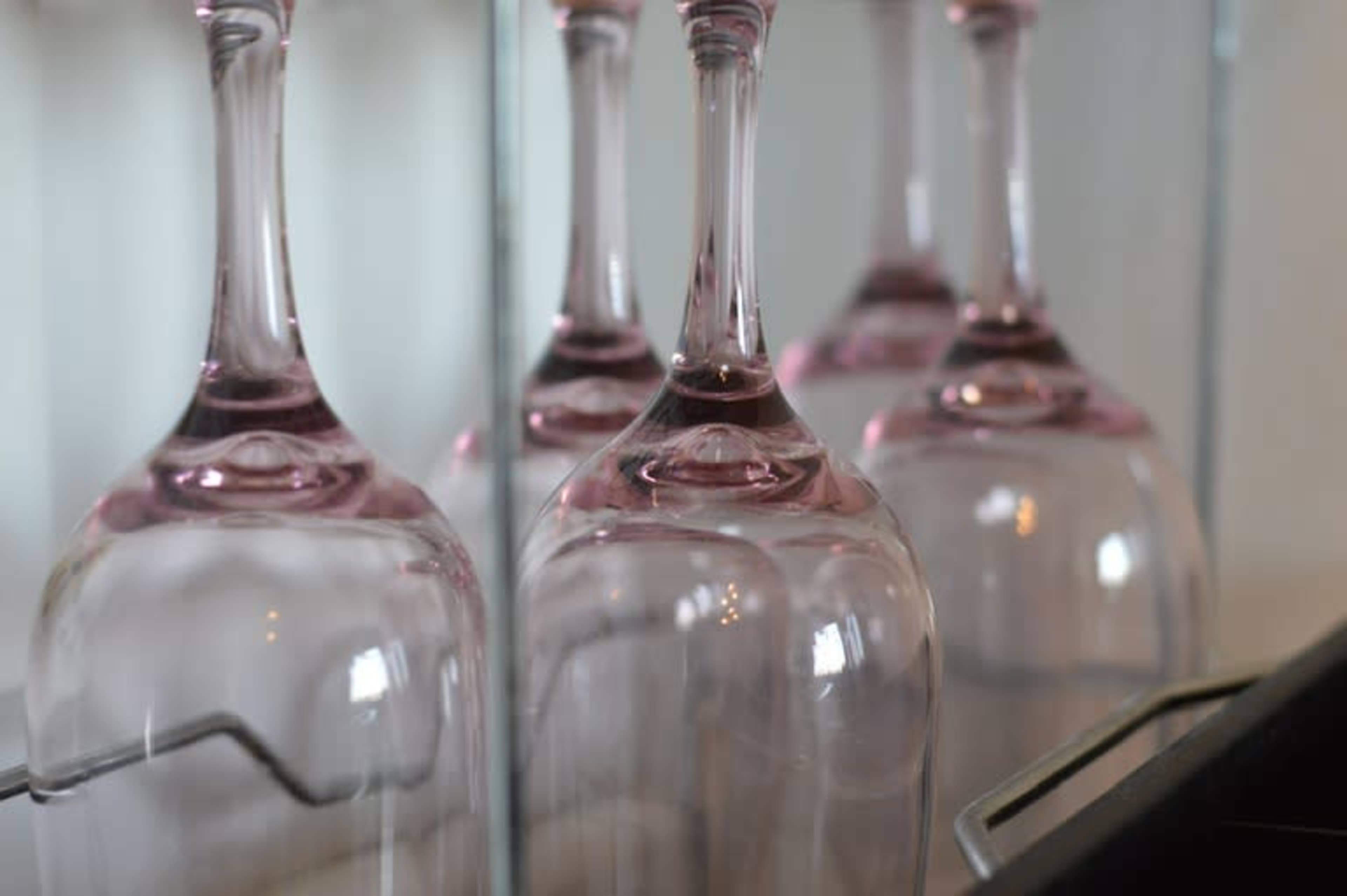 Several upside-down pink-tinted wine glasses arranged on a rack.