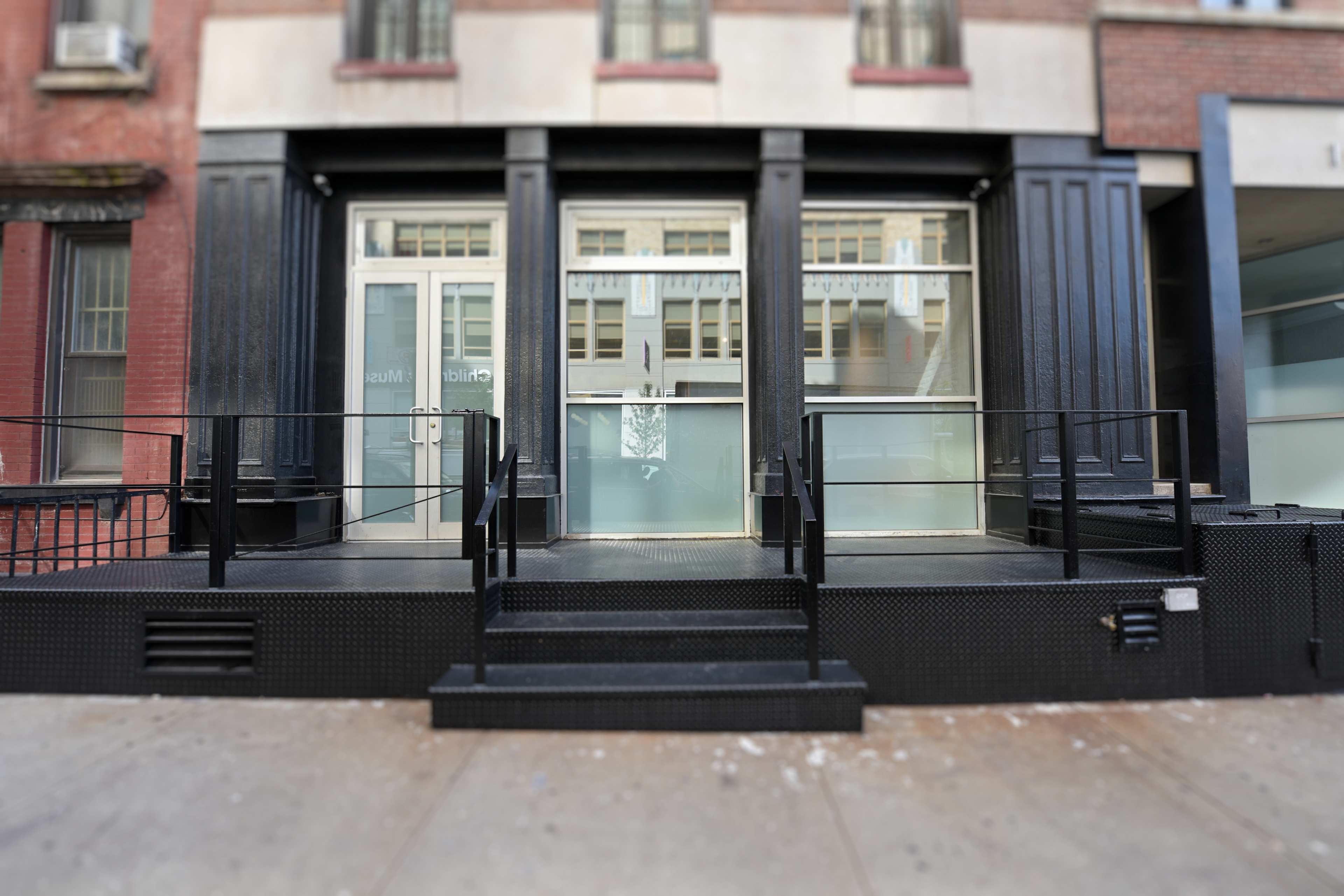 The image shows the entrance of a commercial building with a black exterior and a set of stairs leading up to glass doors.