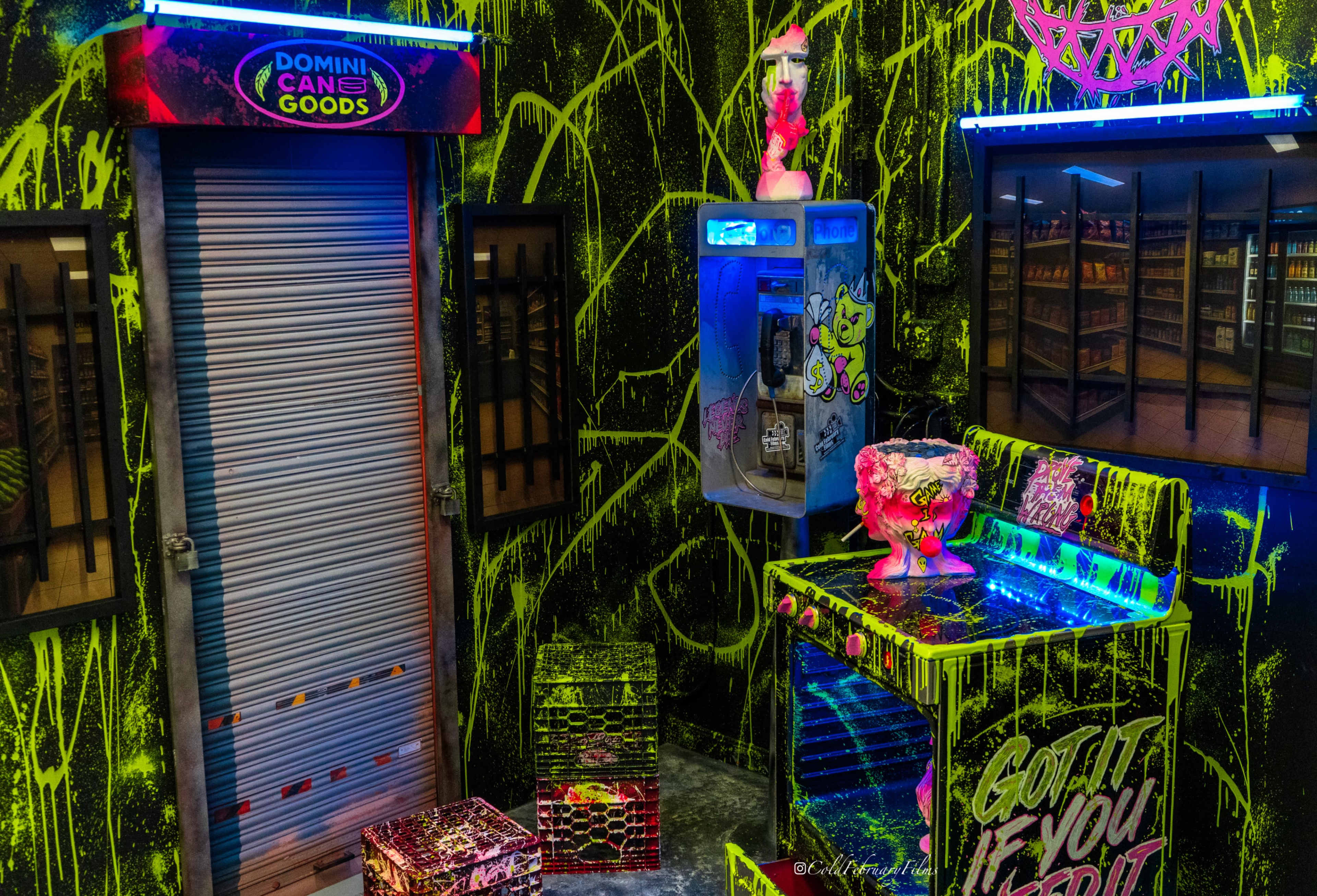 The image displays a vibrant, graffiti-covered arcade scene featuring a closed storefront with a roller shutter, an old-fashioned payphone, and a colorful illuminated countertop with decorative items.