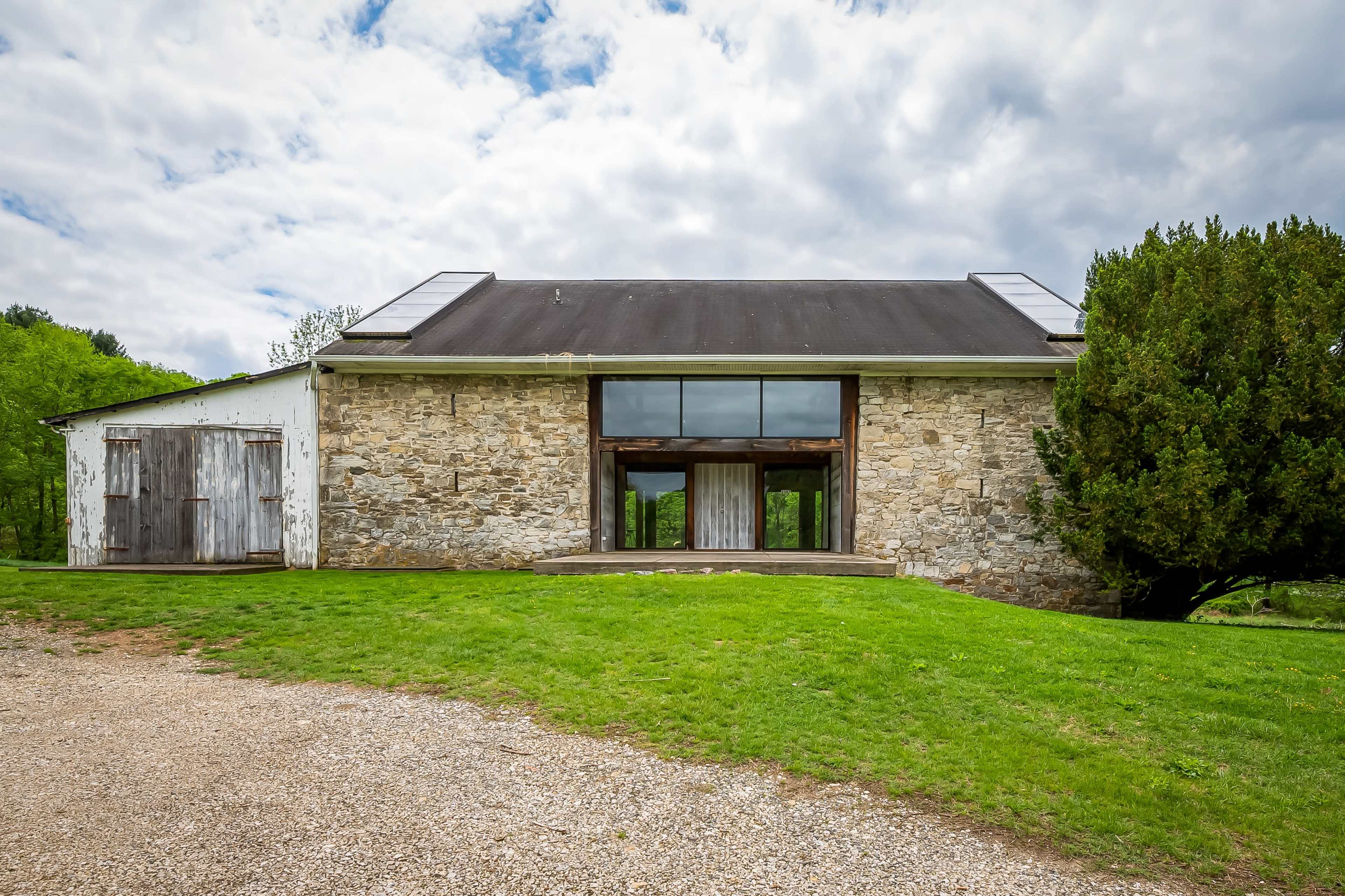 A stone and wooden building with a large glass window is set against a green landscape under a cloudy sky.