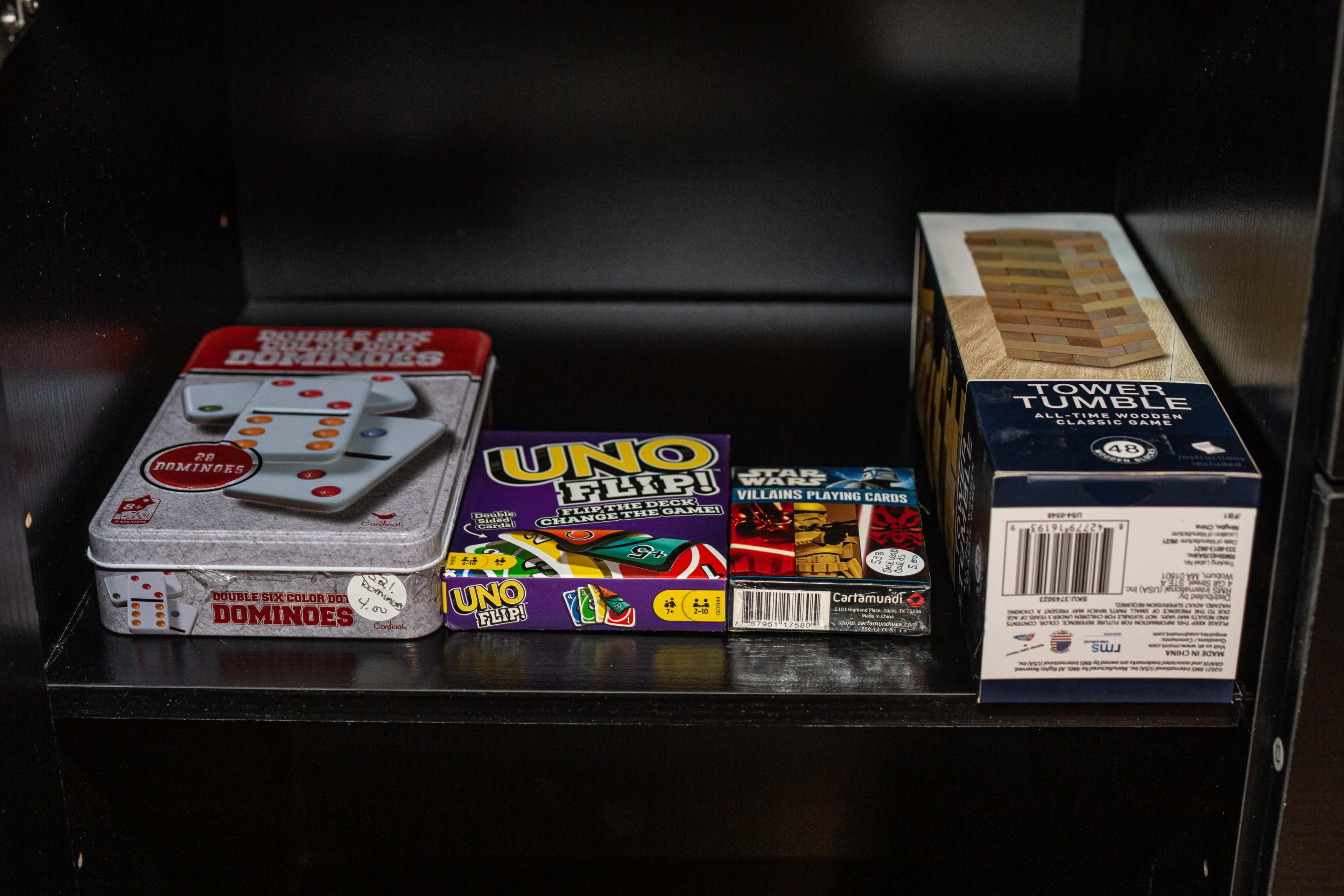 A shelf displays a set of dominoes, a pack of UNO Flip cards, a deck of Star Wars playing cards, and a Tower Tumble game.