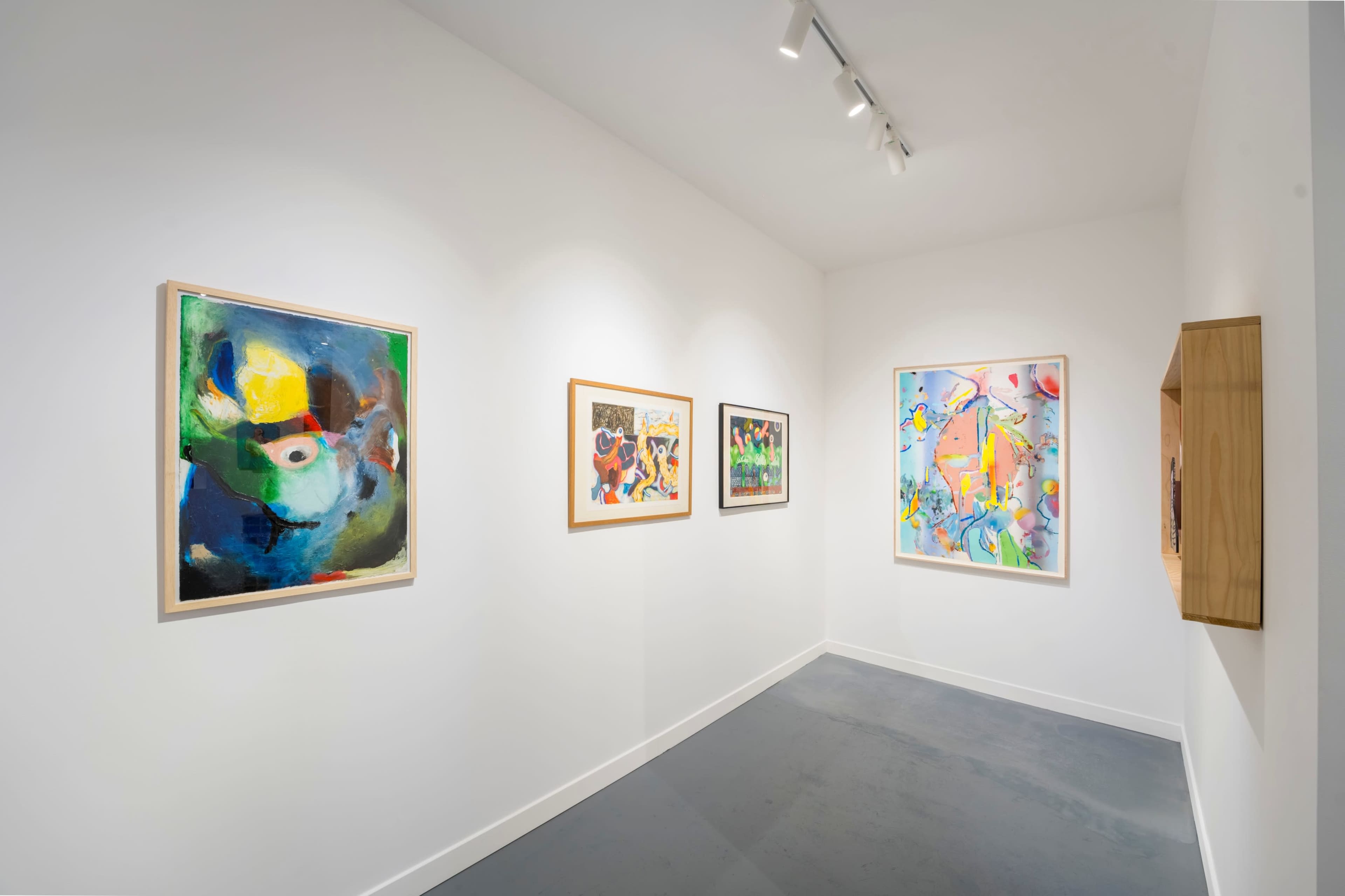 The image shows an art gallery featuring colorful abstract paintings displayed on white walls.