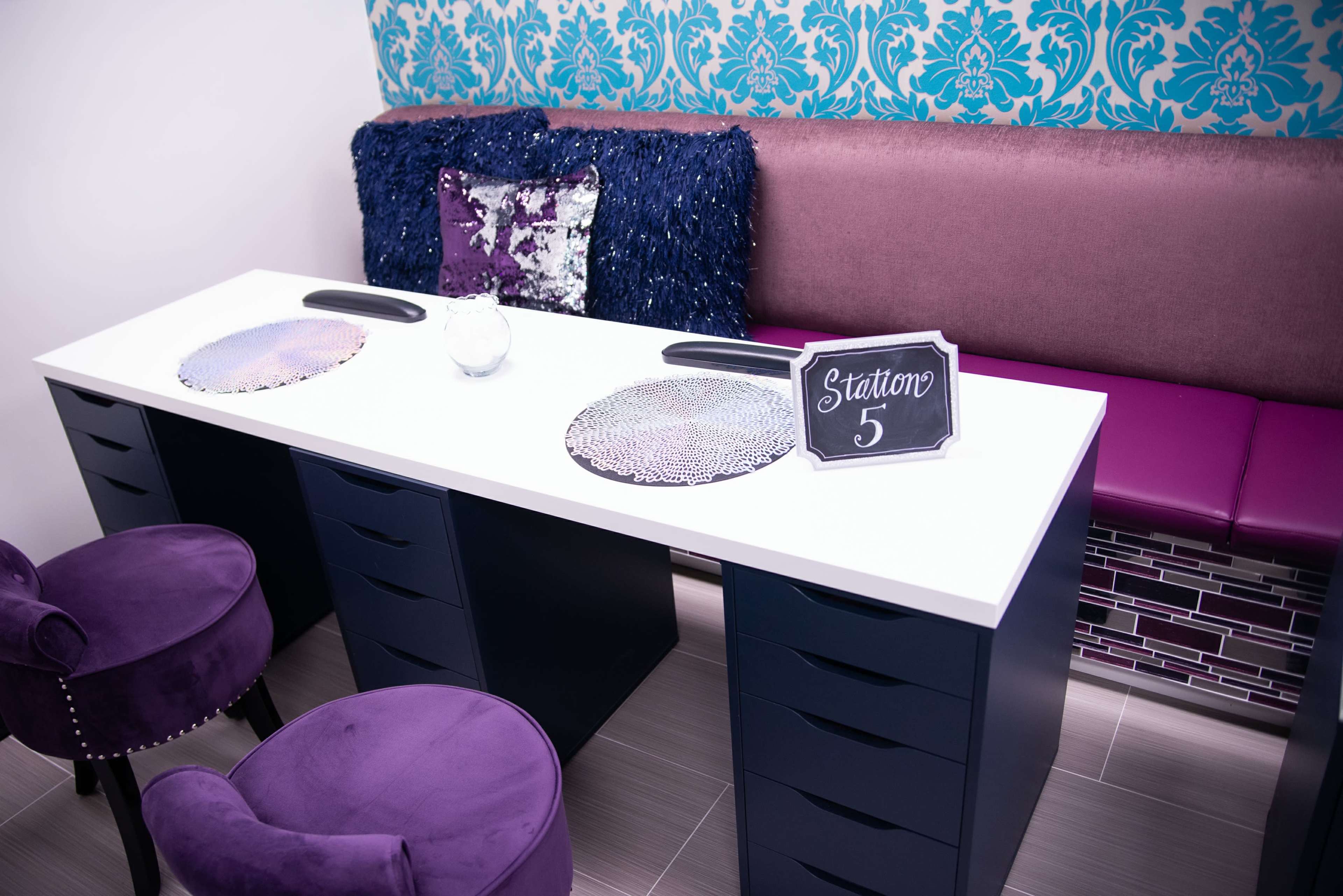 The image shows a nail salon station with two purple chairs, a white countertop, and a sign labeled "Station 5."