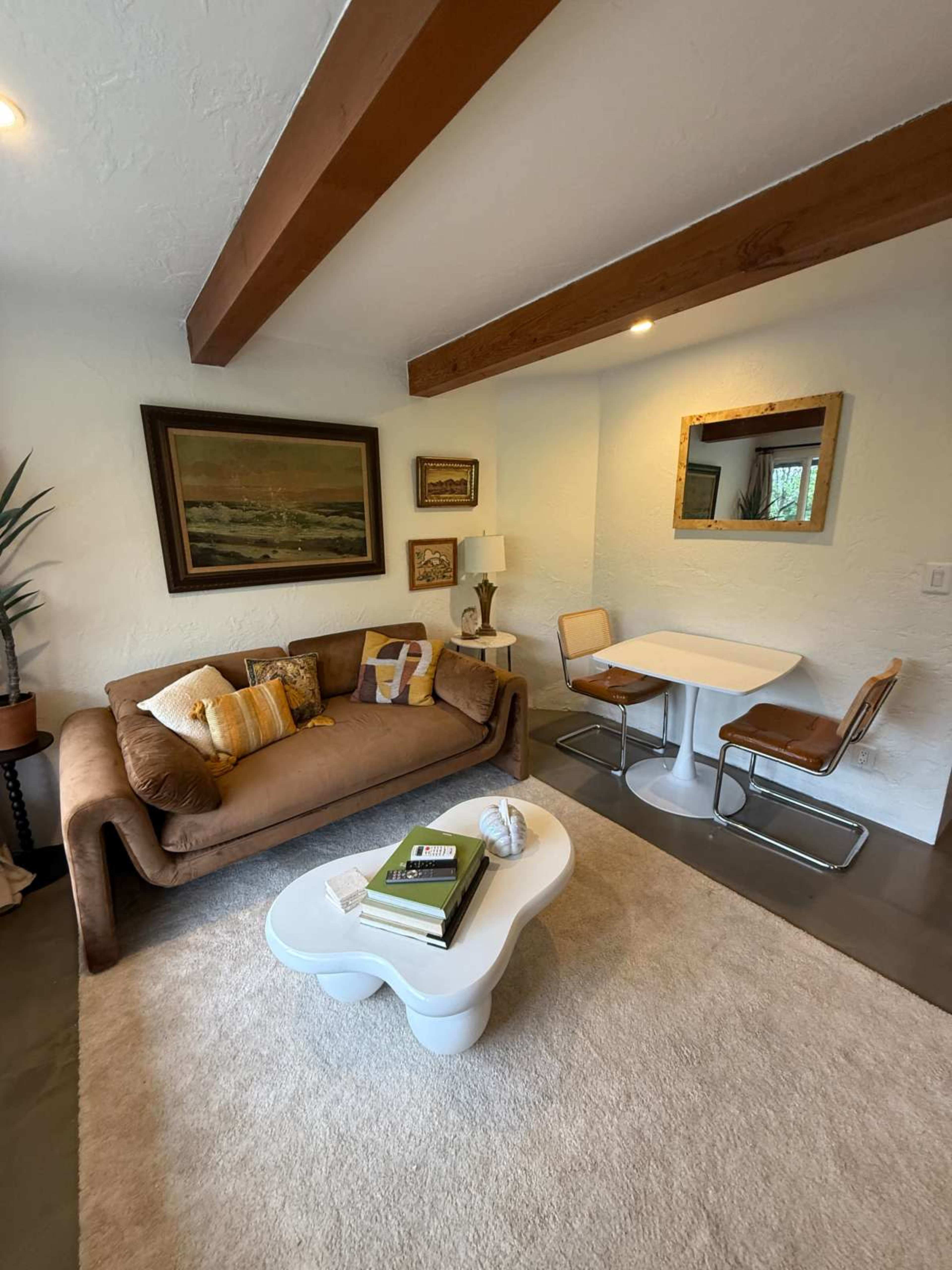The image shows a cozy living space with a brown couch, a white coffee table, and a dining set featuring two chairs and a small table.