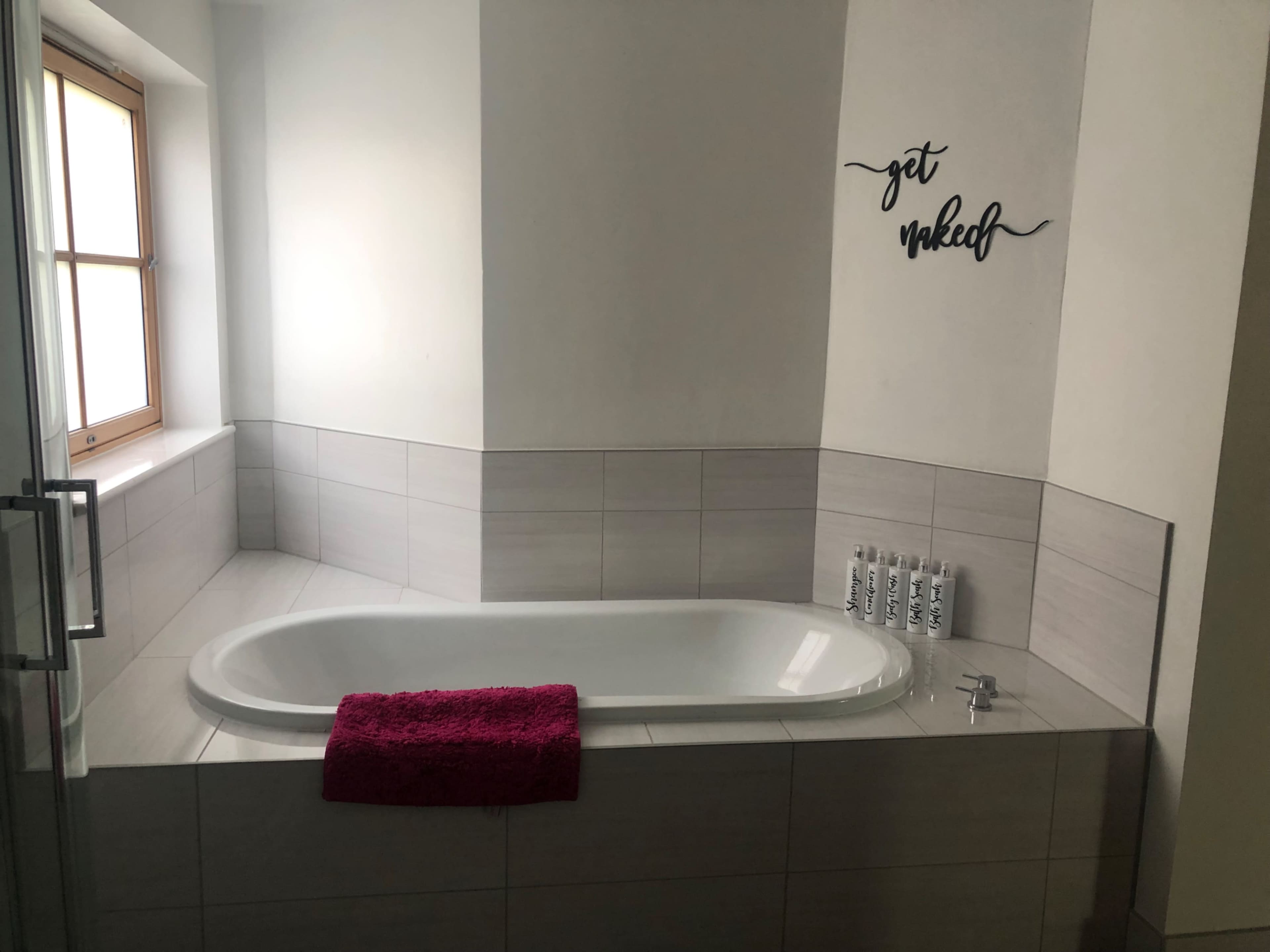 A modern bathroom with a bathtub, a pink towel, and a wall decal that says "get naked."