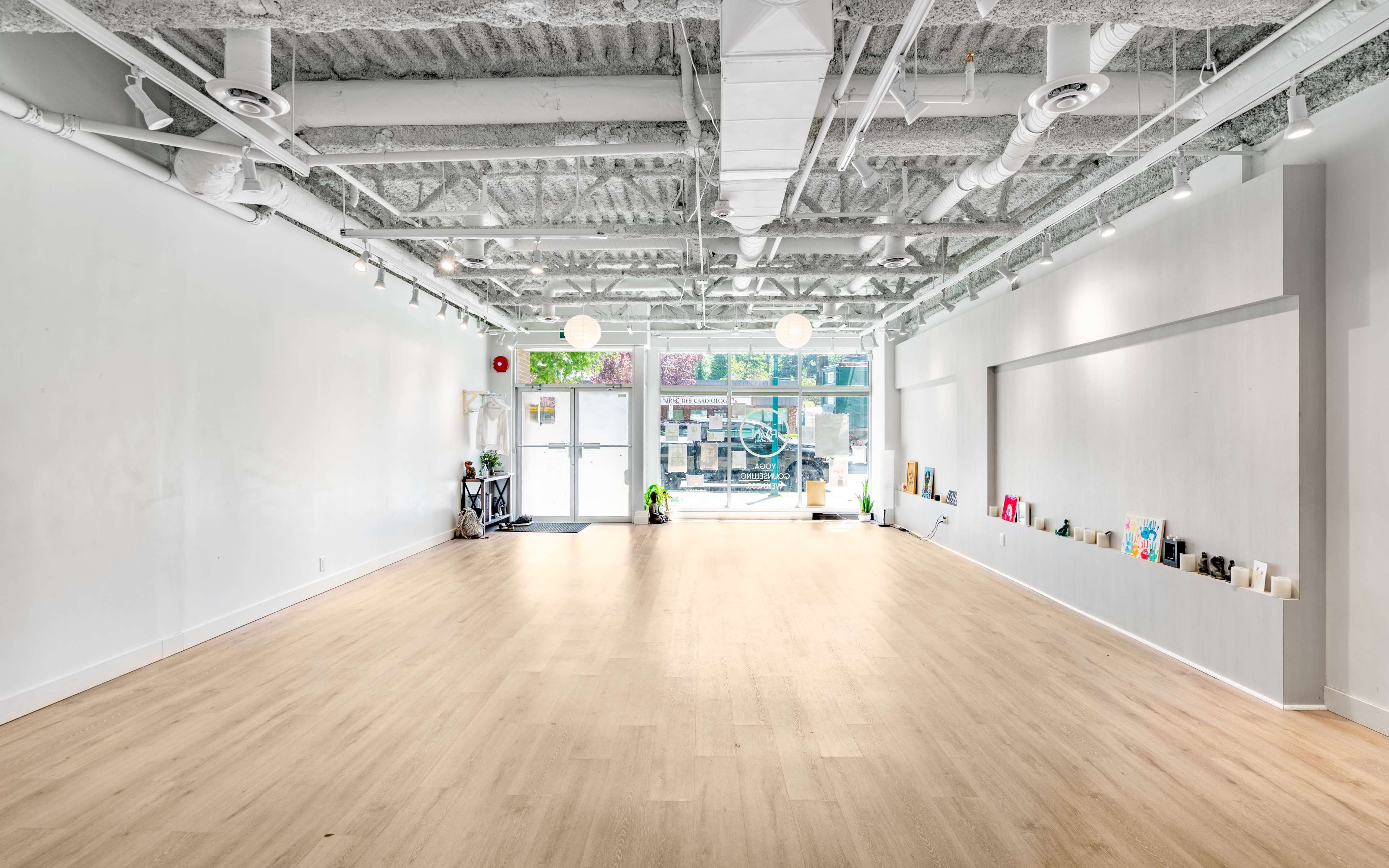 A spacious, empty interior of a modern studio with white walls and wooden flooring, illuminated by natural light from large windows.