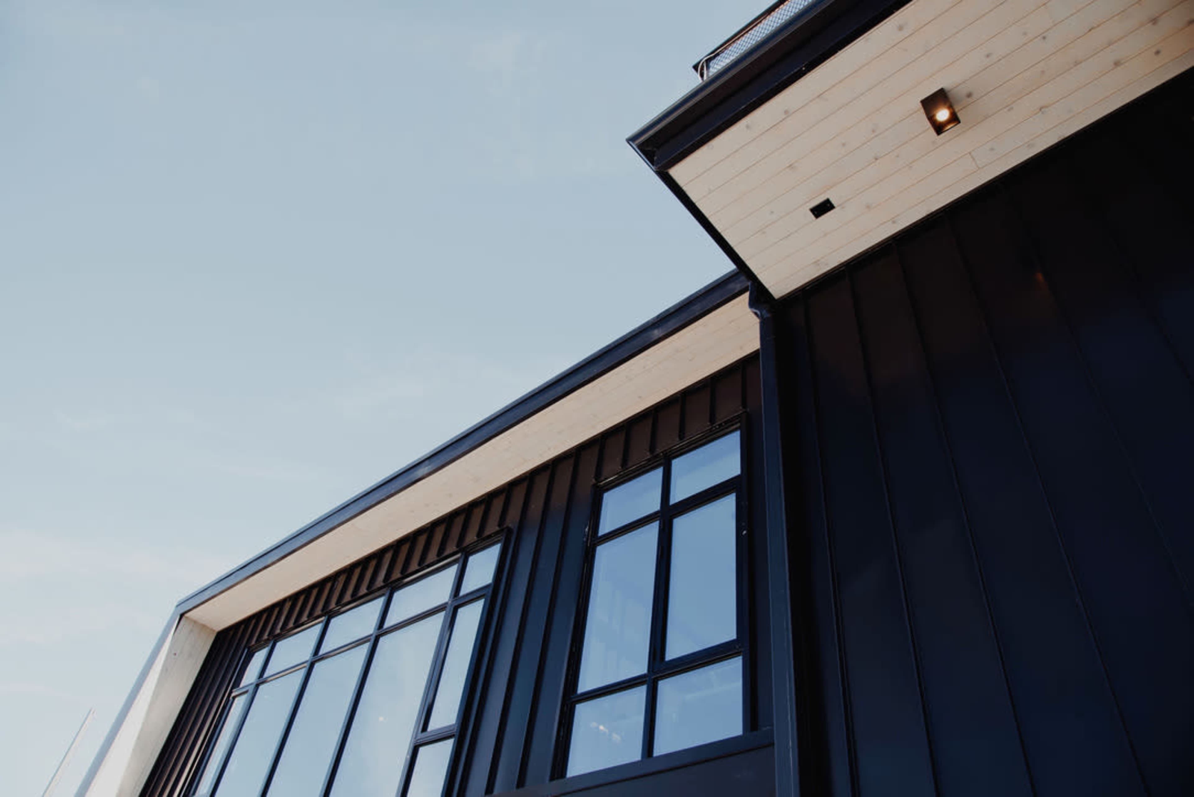 The image shows a modern building with large windows and a black exterior facade against a clear sky.