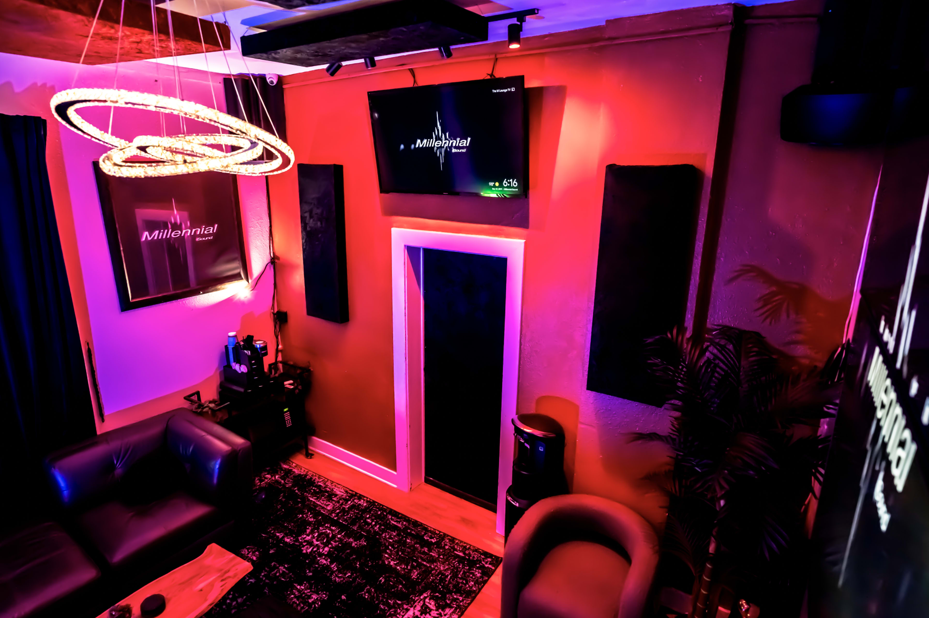A modern room with a dark color scheme, featuring a television on the wall, a couch, and a circular light fixture.