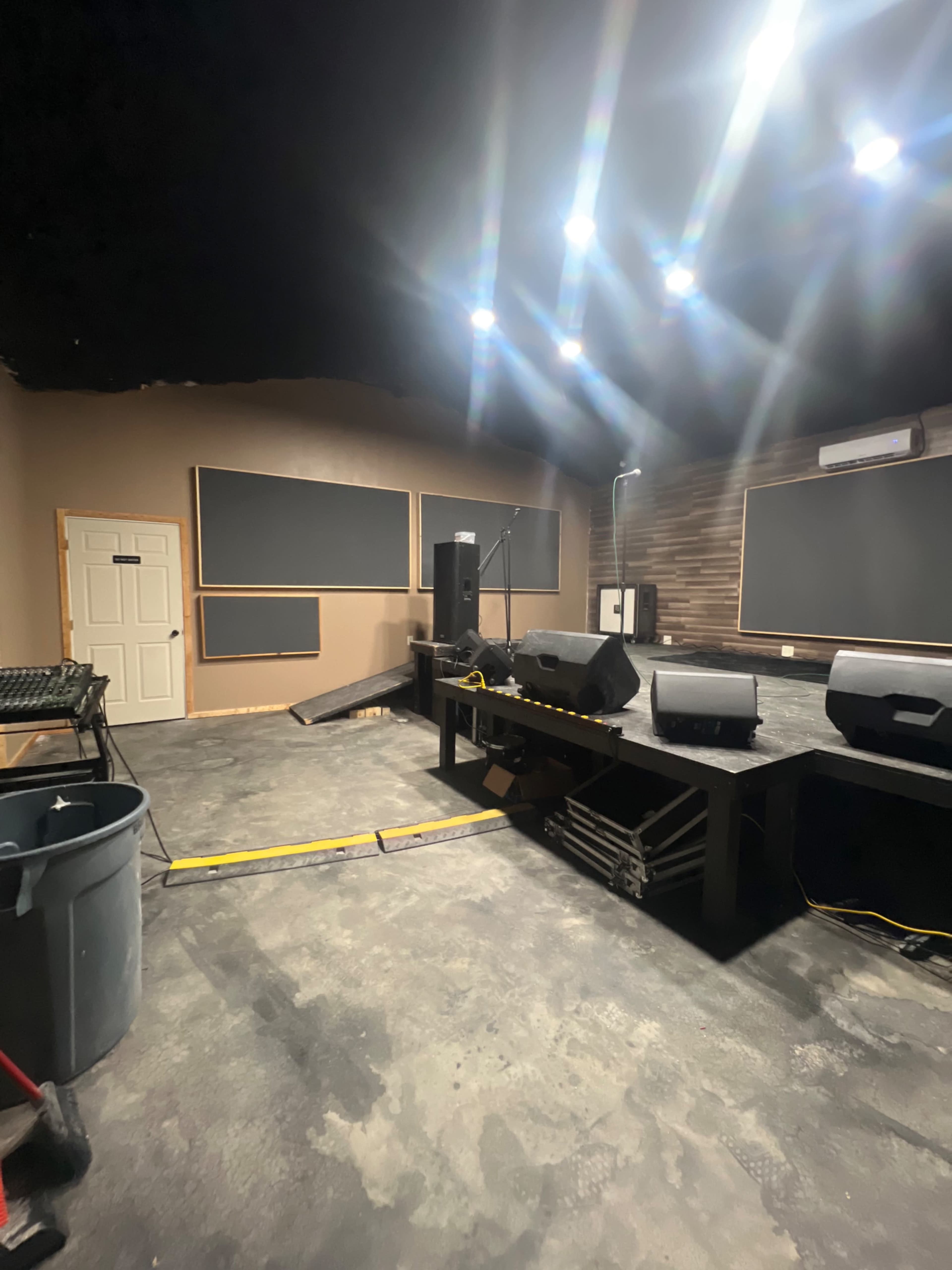 A music studio space with soundproofing panels on the walls, a stage with speakers, and various audio equipment.