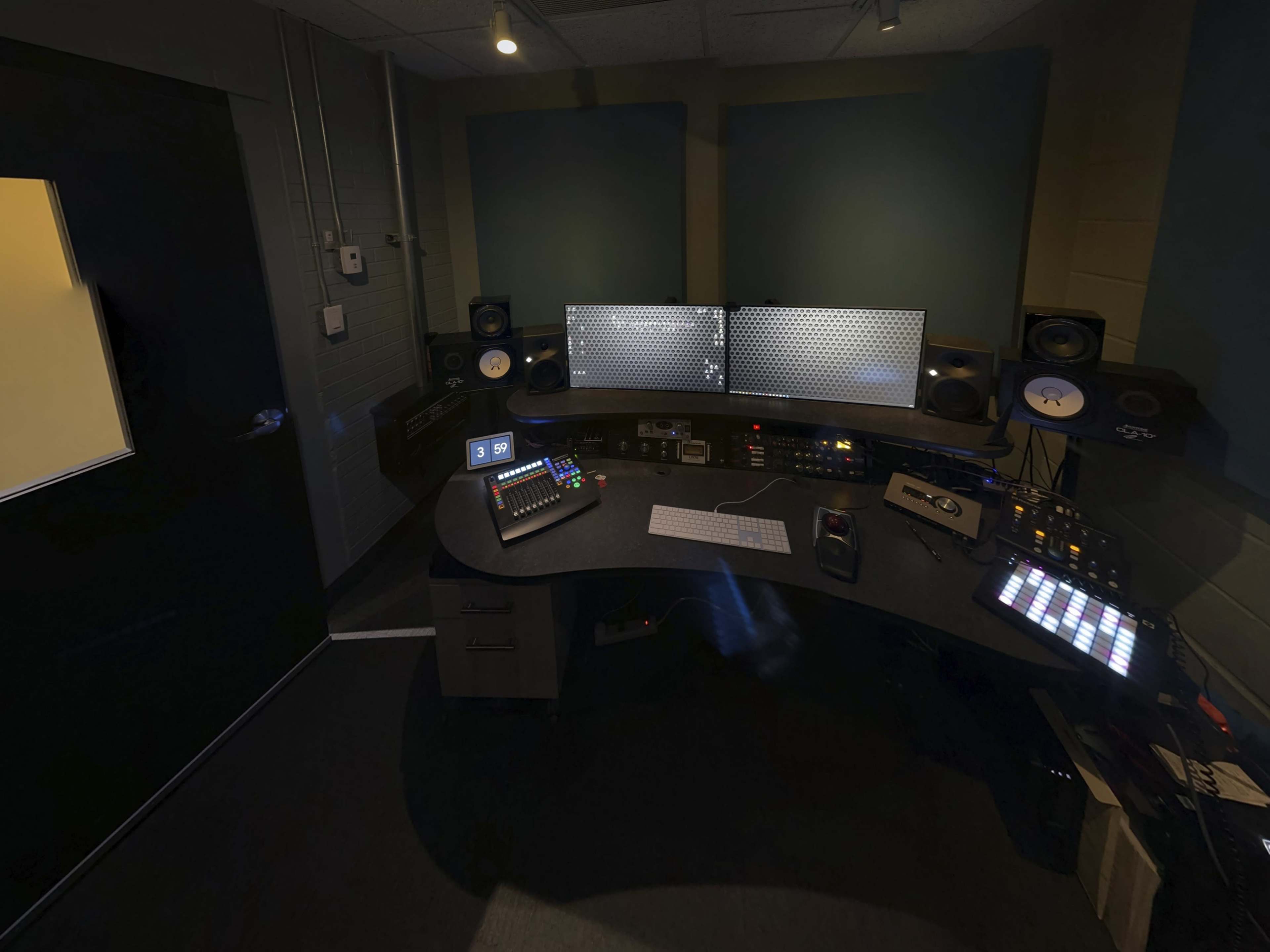 A music production studio featuring a curved desk with multiple monitors, audio equipment, and sound speakers in a dimly lit room.