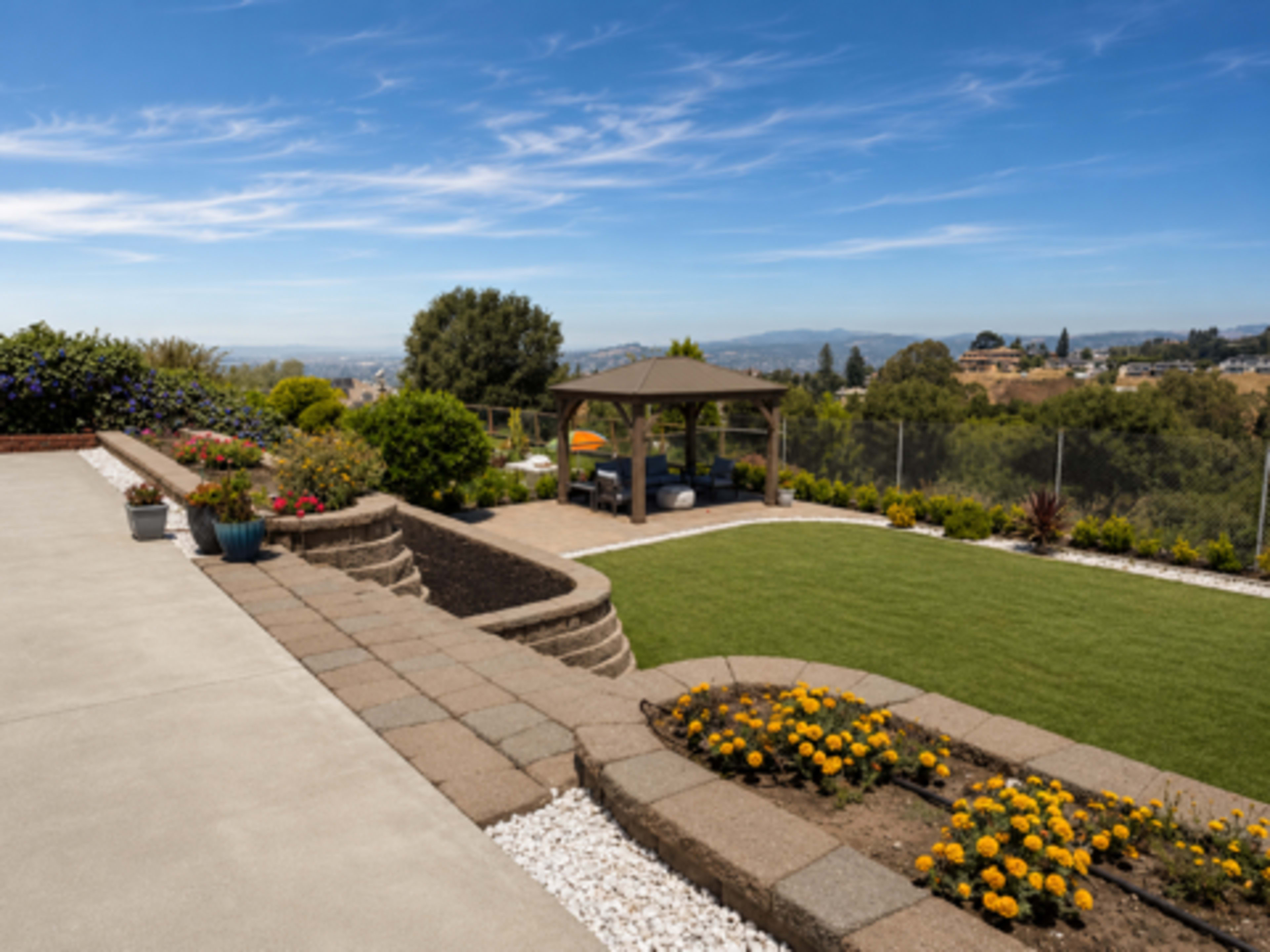 The image shows a landscaped backyard featuring a gazebo, a manicured lawn, and flowerbeds with colorful blooms, all set against a scenic view of rolling hills.
