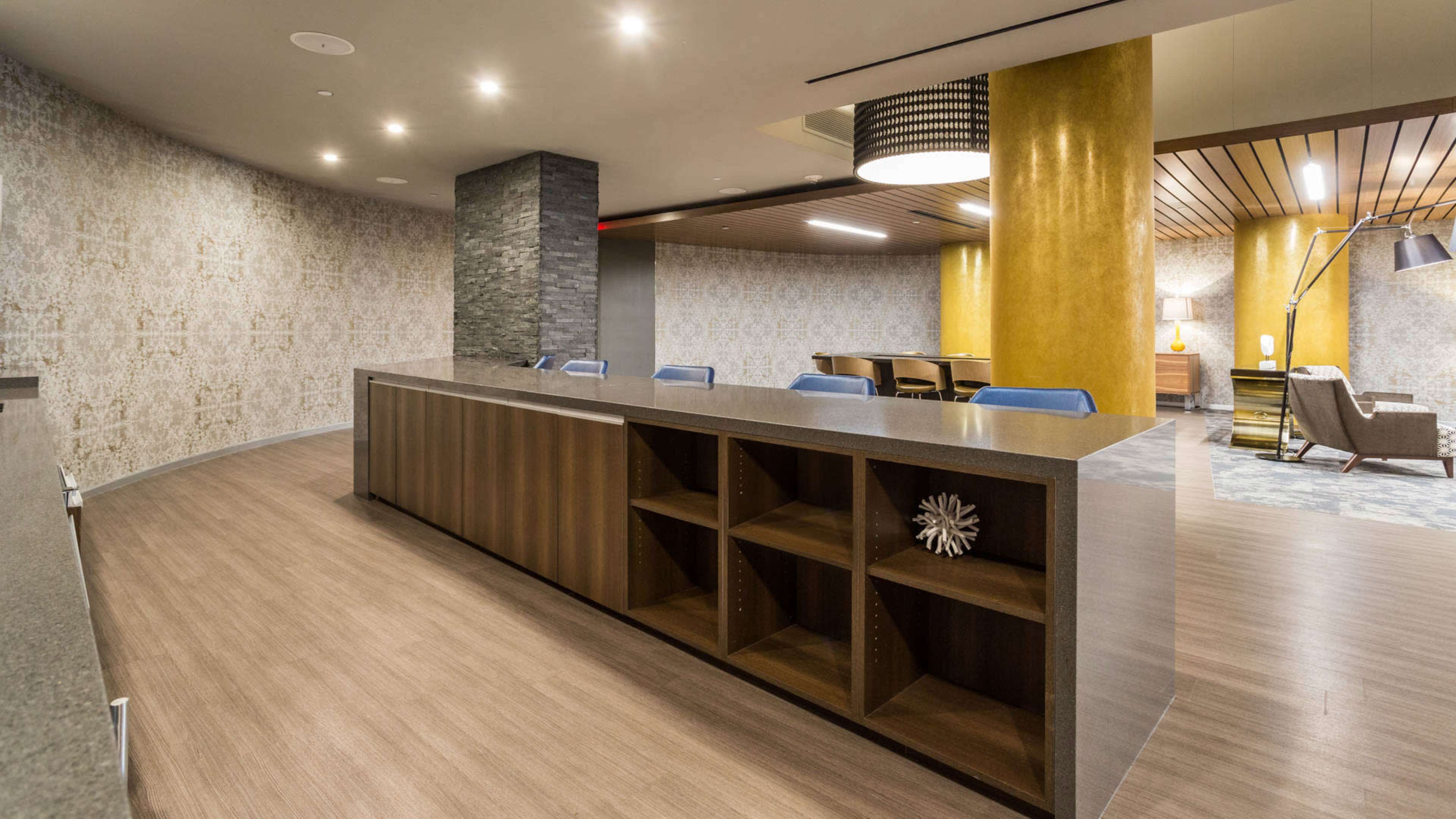 A modern reception area features a curved front desk, wooden flooring, and decorative wall elements with yellow and gray tones.