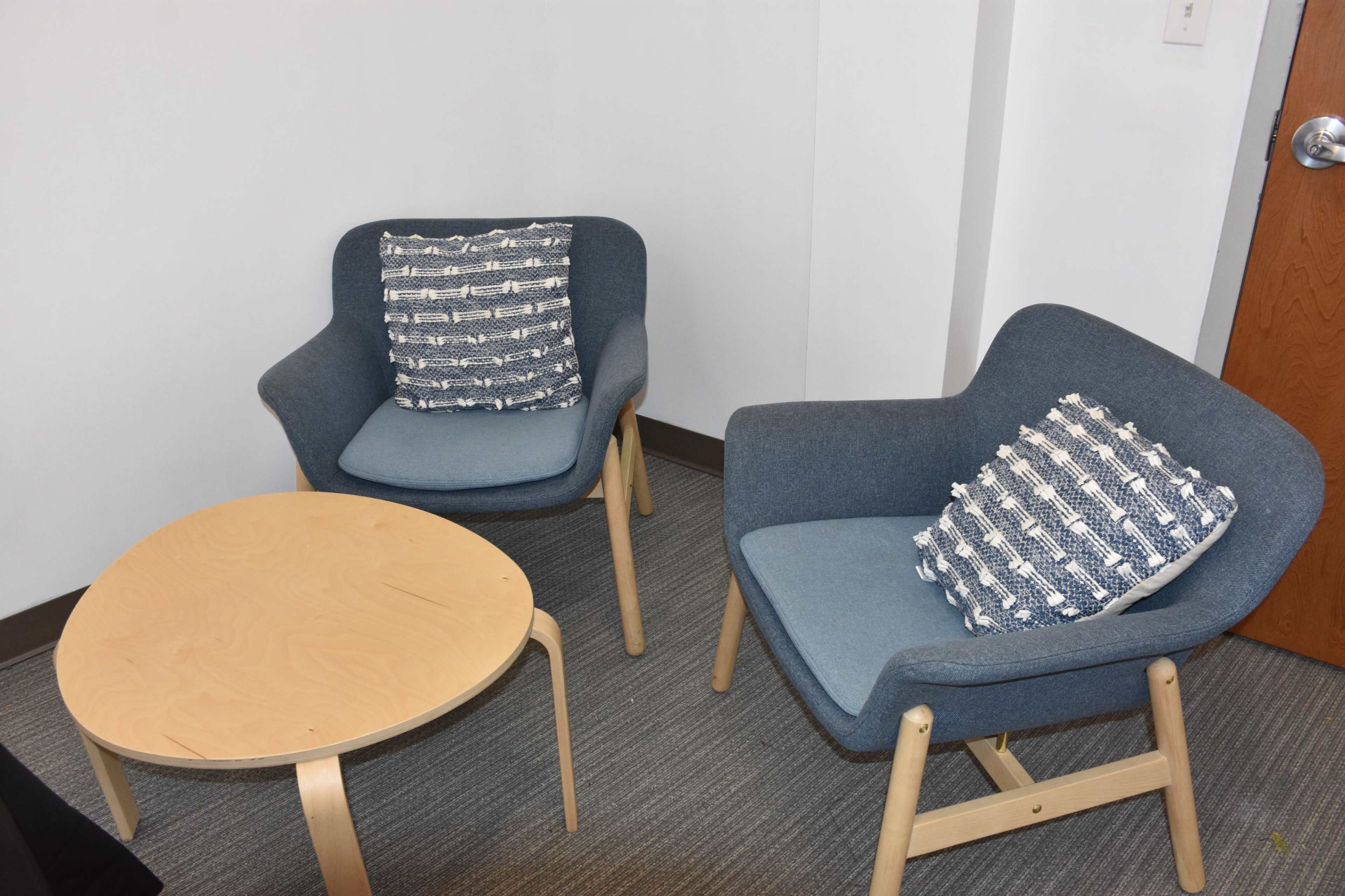 The image shows two blue armchairs with patterned cushions flanking a small wooden table in a neutral-toned room.