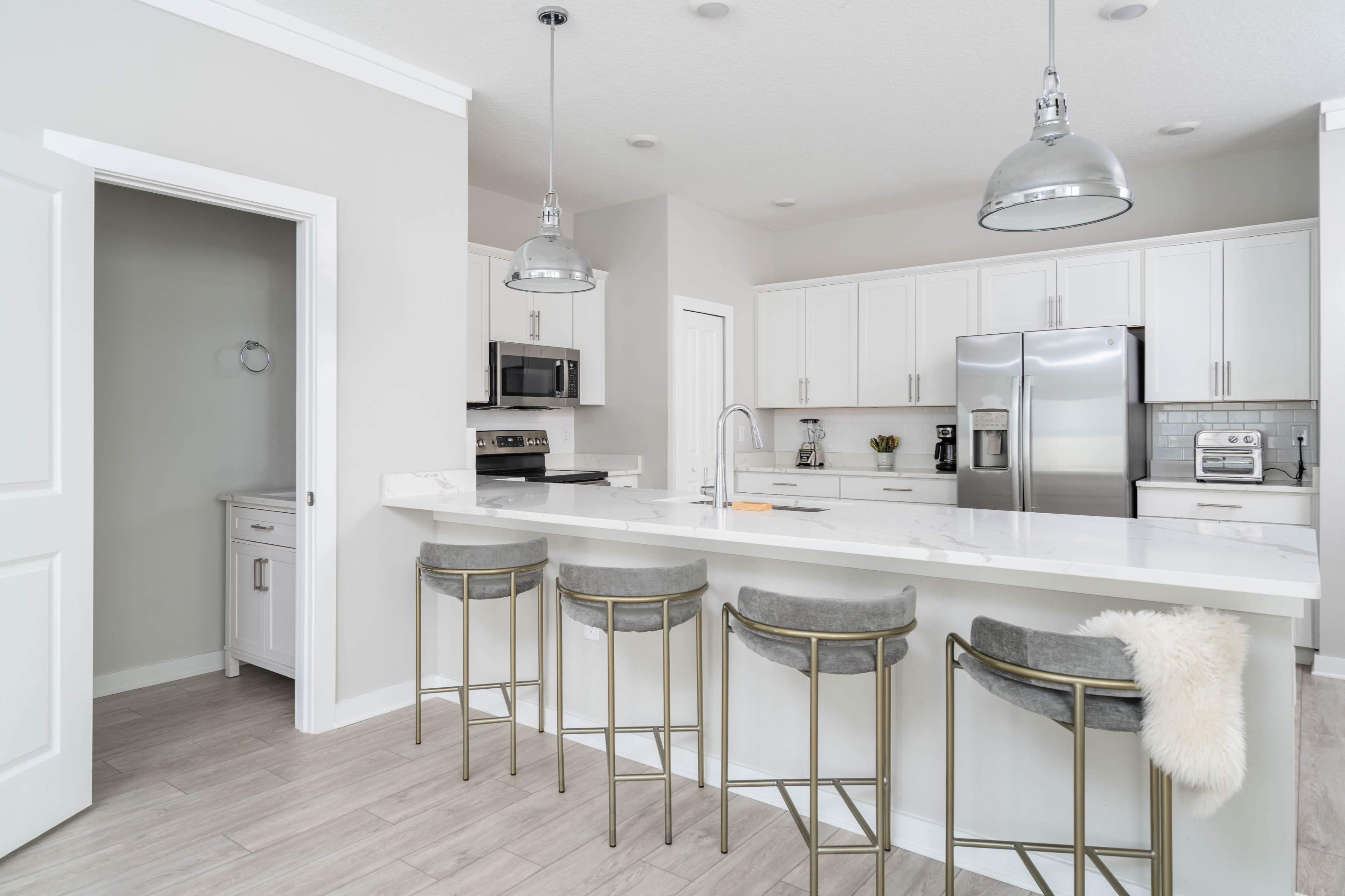 A modern kitchen featuring a large island with gray bar stools, stainless steel appliances, and white cabinetry.