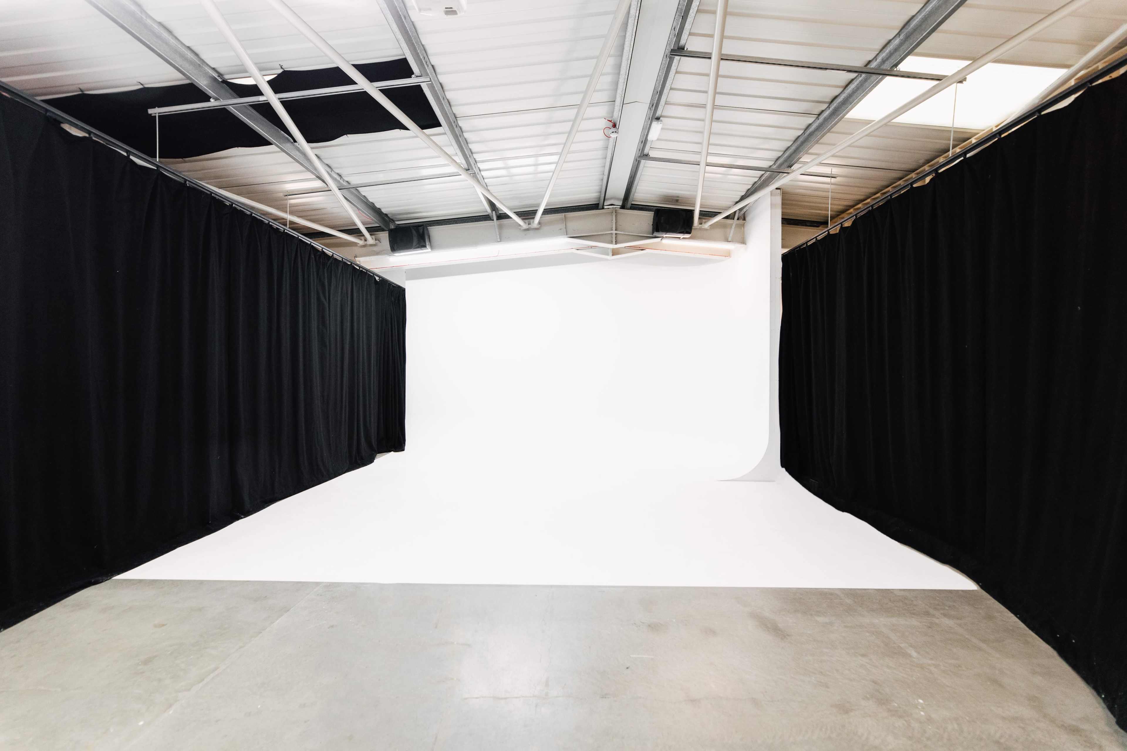 The image shows a spacious photography studio with white seamless paper and black curtains on either side.