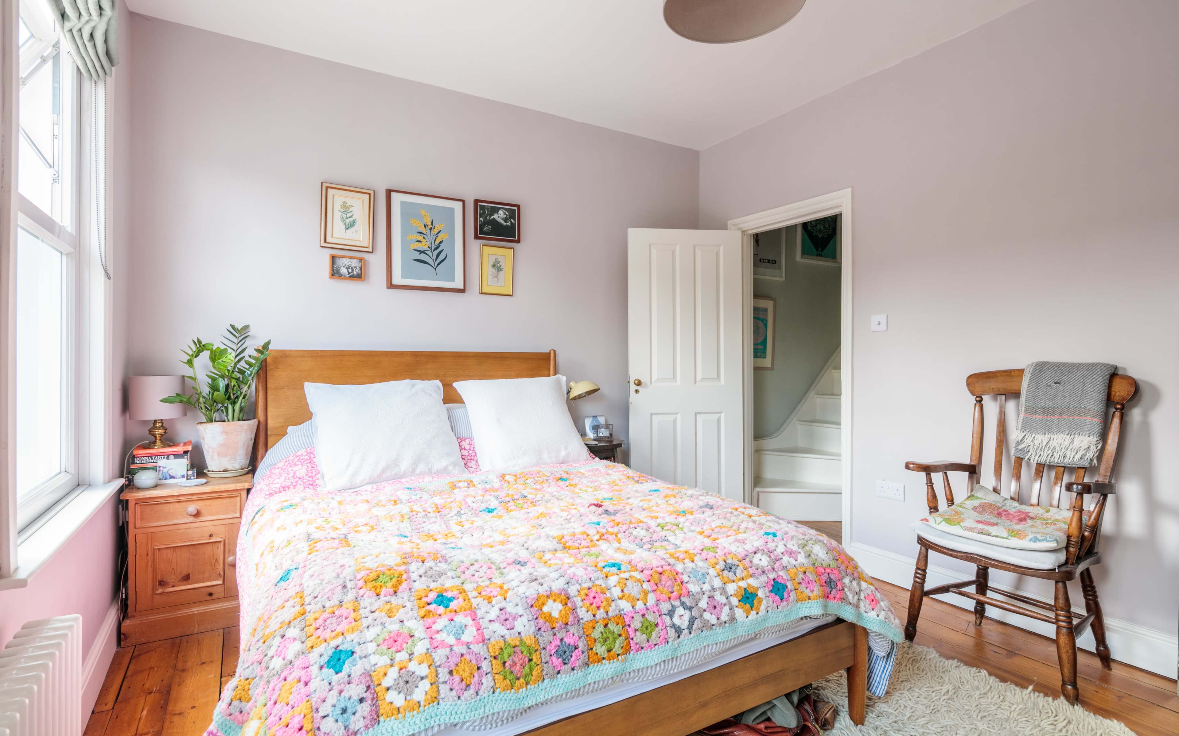 The bedroom features a wooden bed with a brightly colored crocheted blanket, framed artwork on the walls, and a rocking chair in the corner.