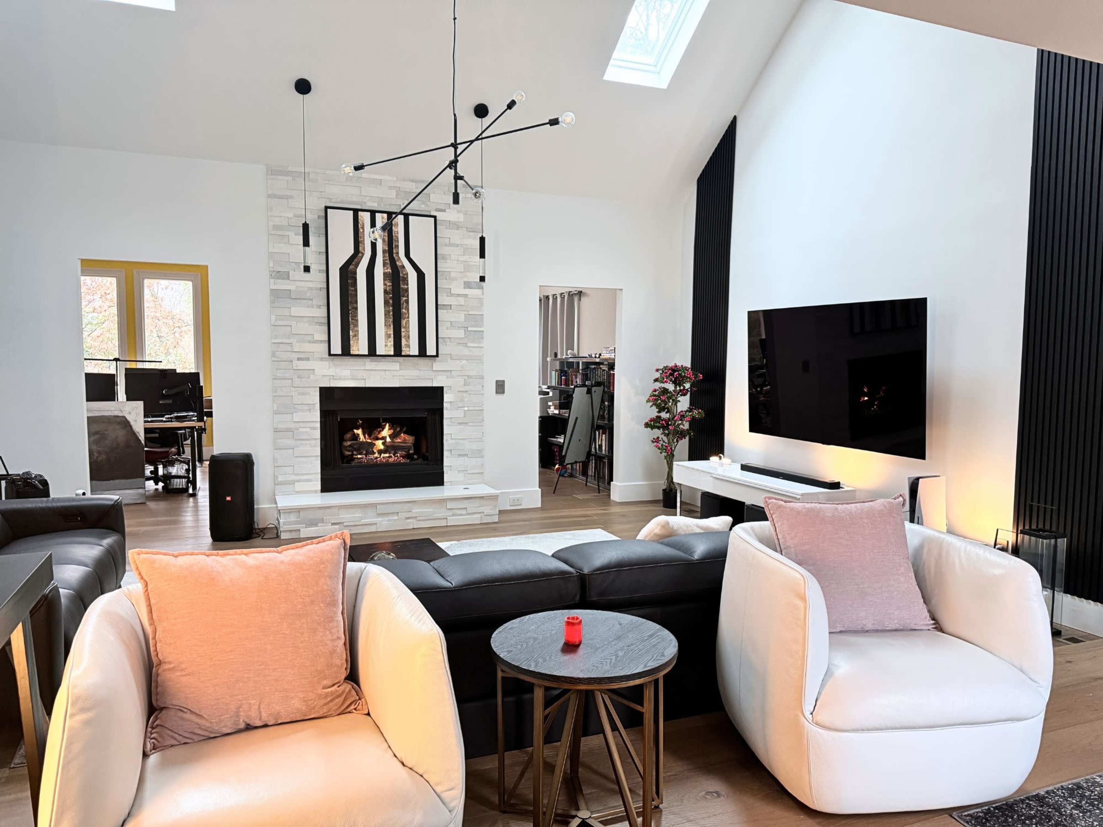 The room features a modern living space with a fireplace, white stone wall, black furniture, and contemporary lighting.