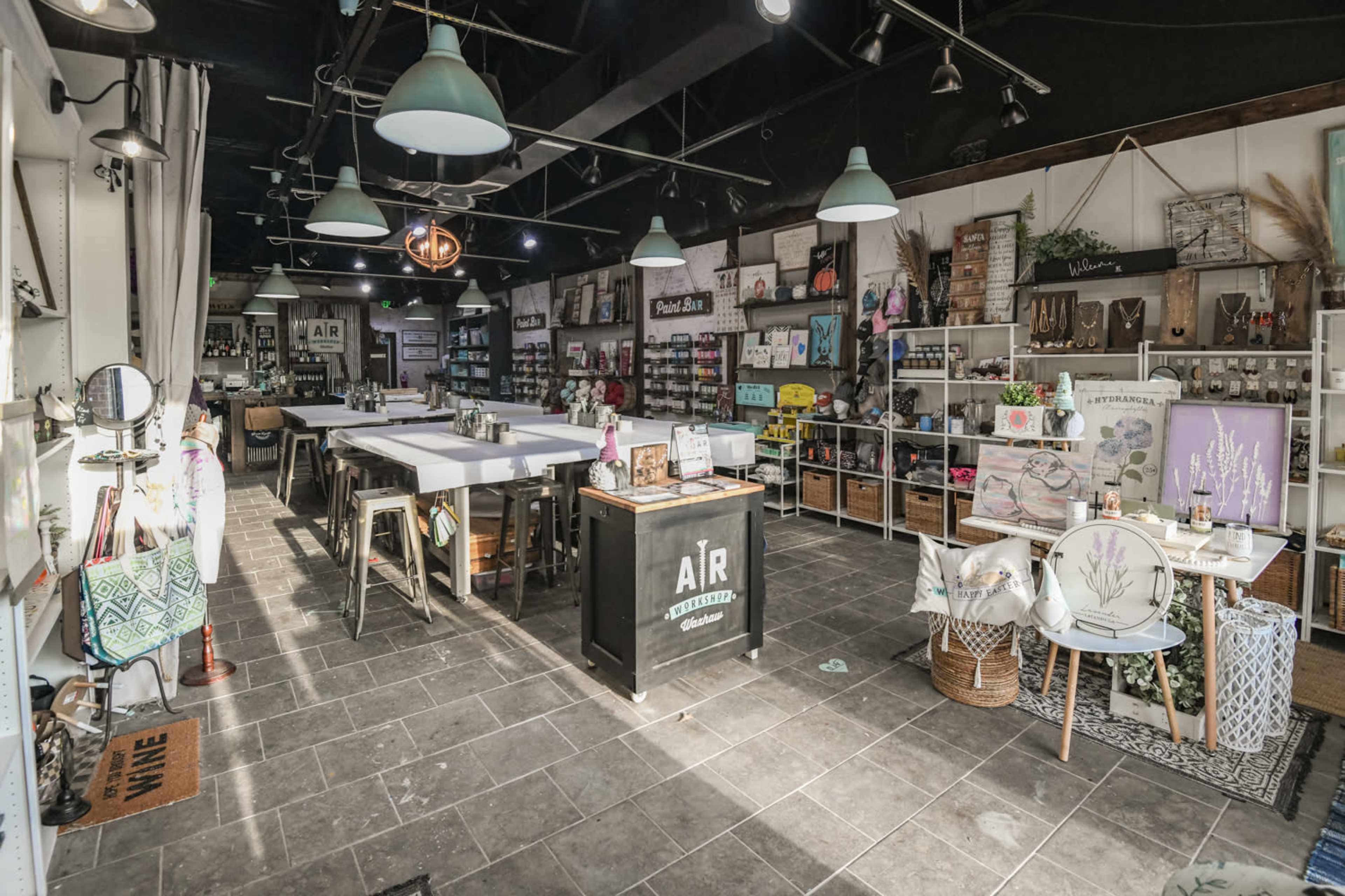 A well-organized craft and vintage store featuring tables for workshops and various decorative items displayed on shelves.