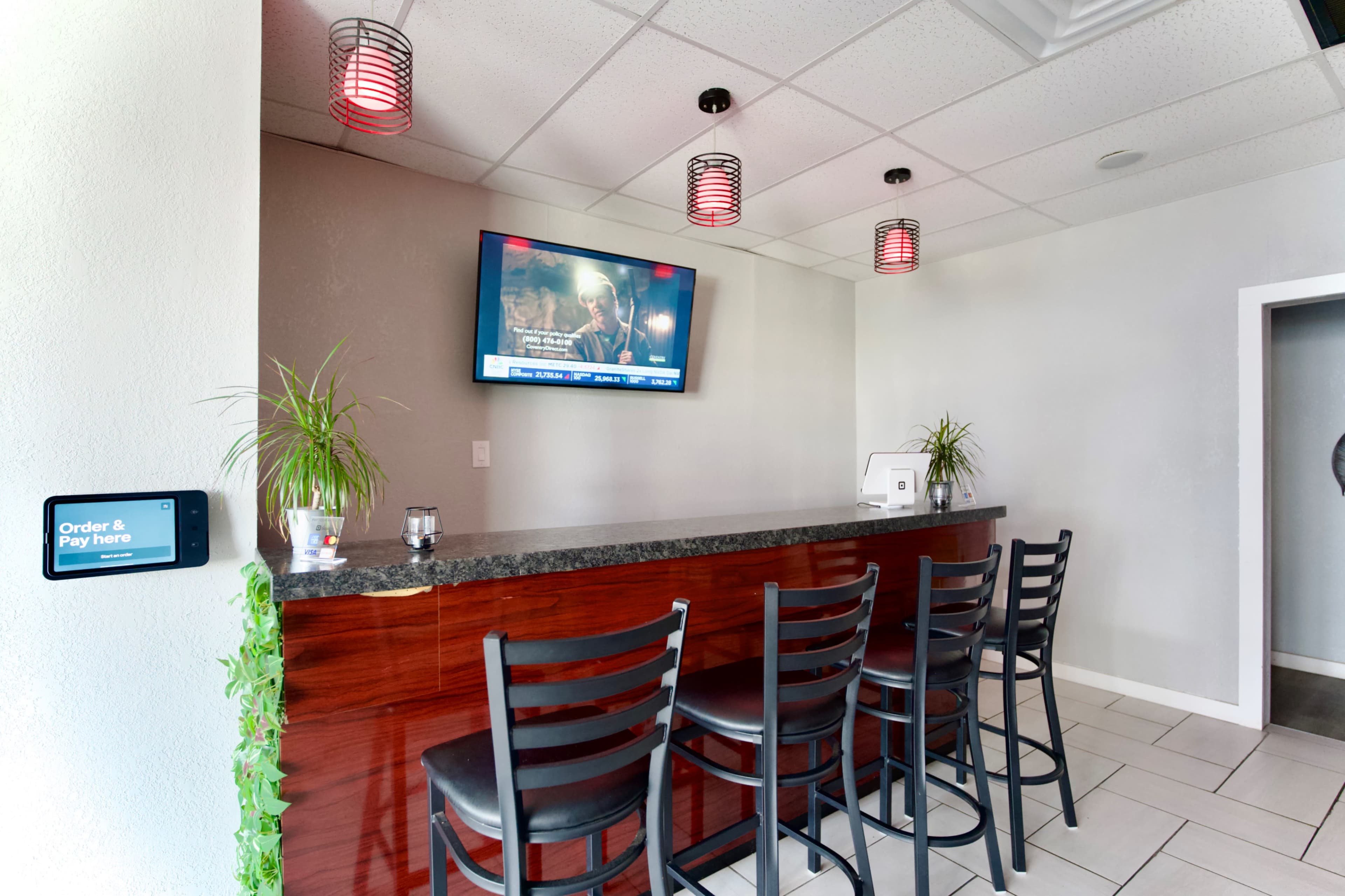 A bar area features a dark wooden countertop with several bar stools, a television mounted on the wall, and pendant lighting overhead.