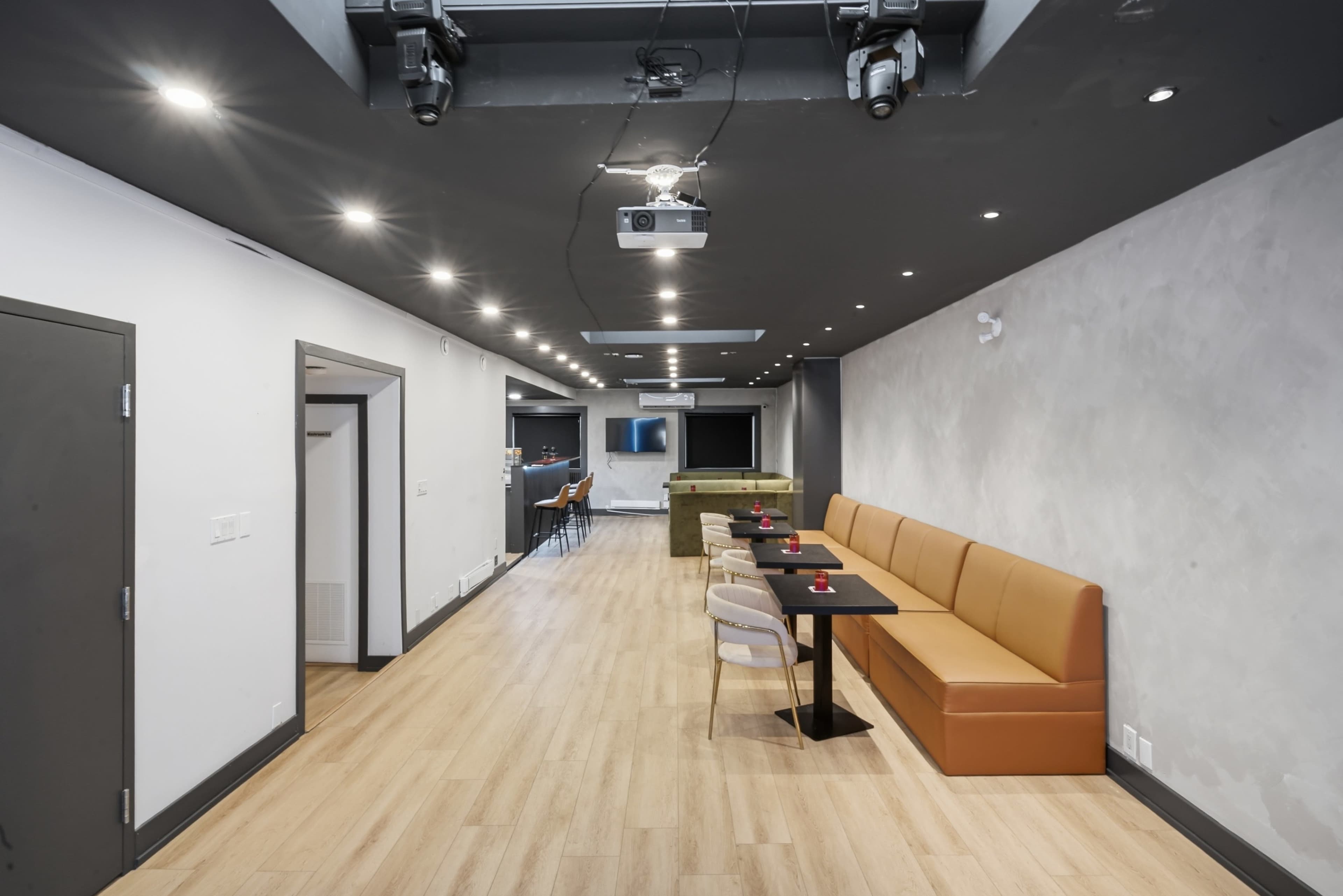 The image shows a modern, spacious room with a long sofa against one wall, a table, and a projection system mounted on the ceiling.
