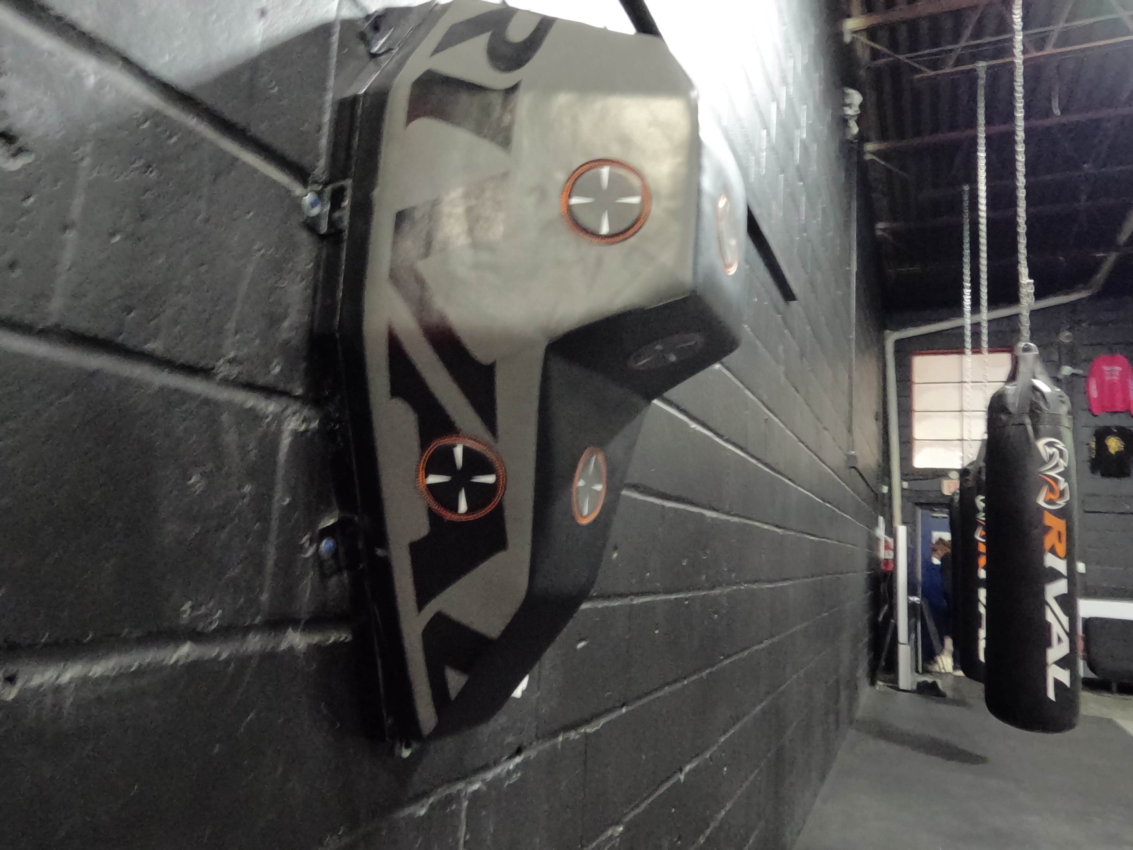 The image shows a black wall-mounted target used for boxing training, with several striking points highlighted.