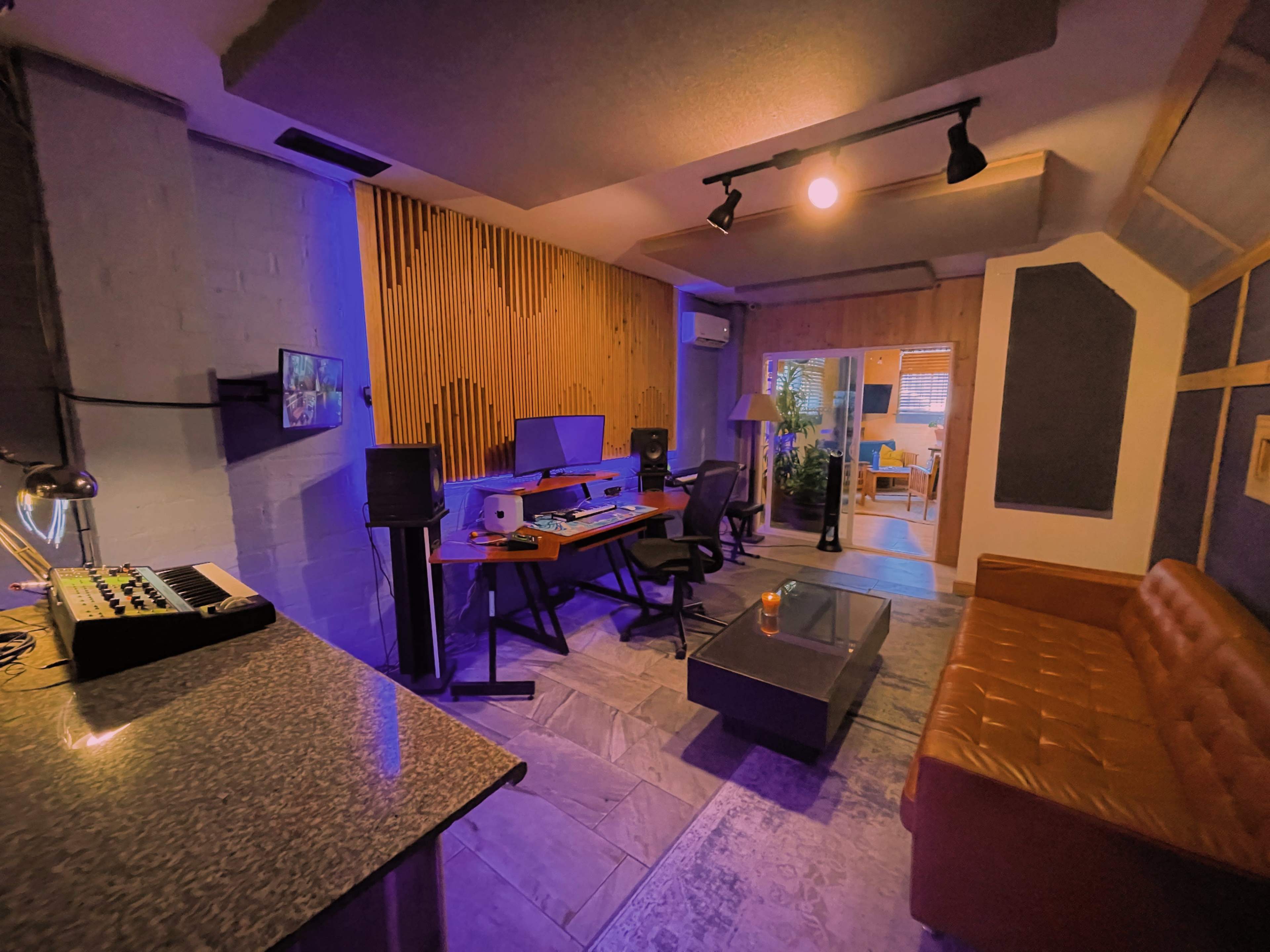 A modern music studio with wooden paneling, a computer setup, and a brown leather sofa.