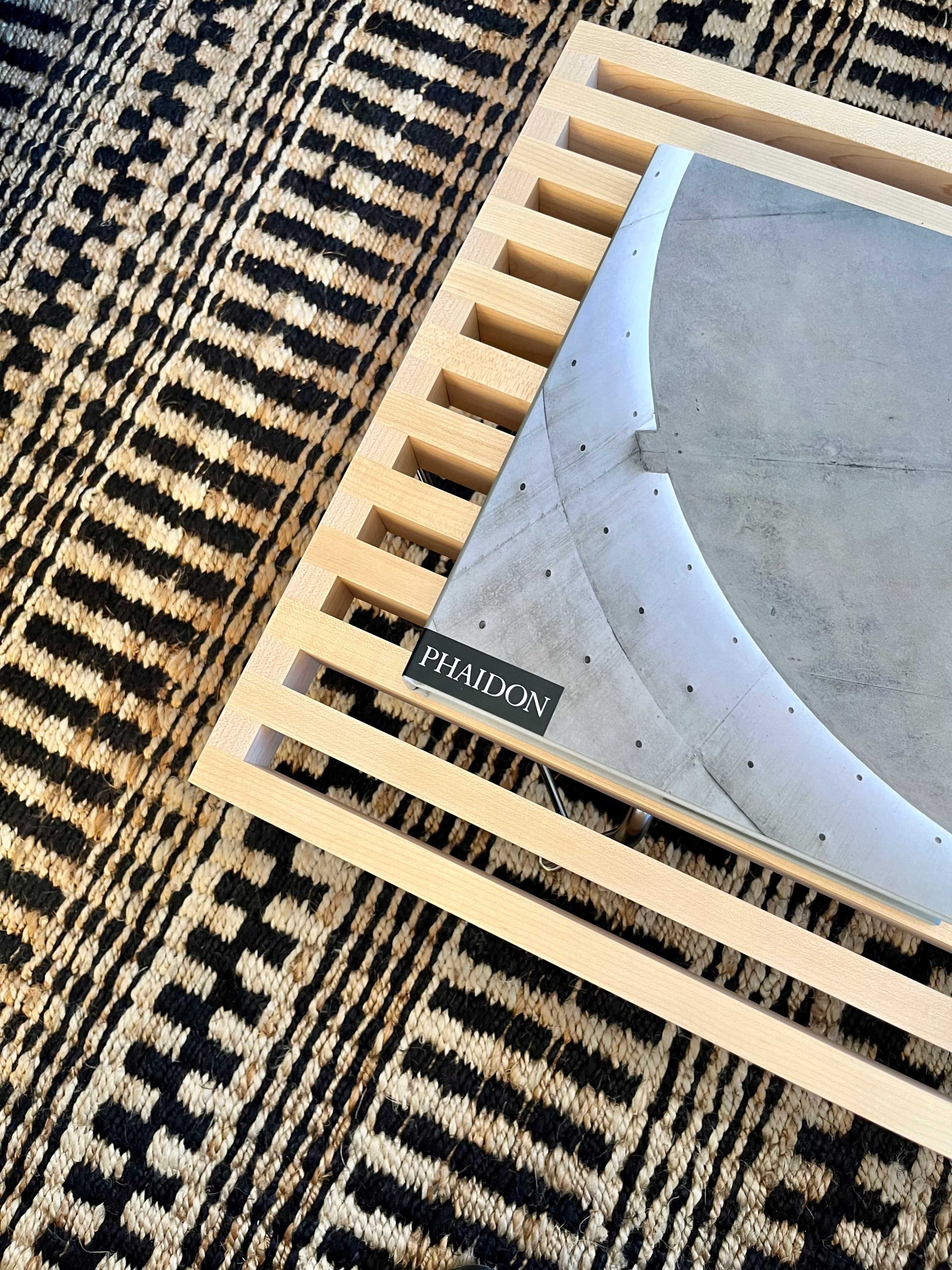 A wooden tray holds a Phaidon book on a geometric patterned rug.