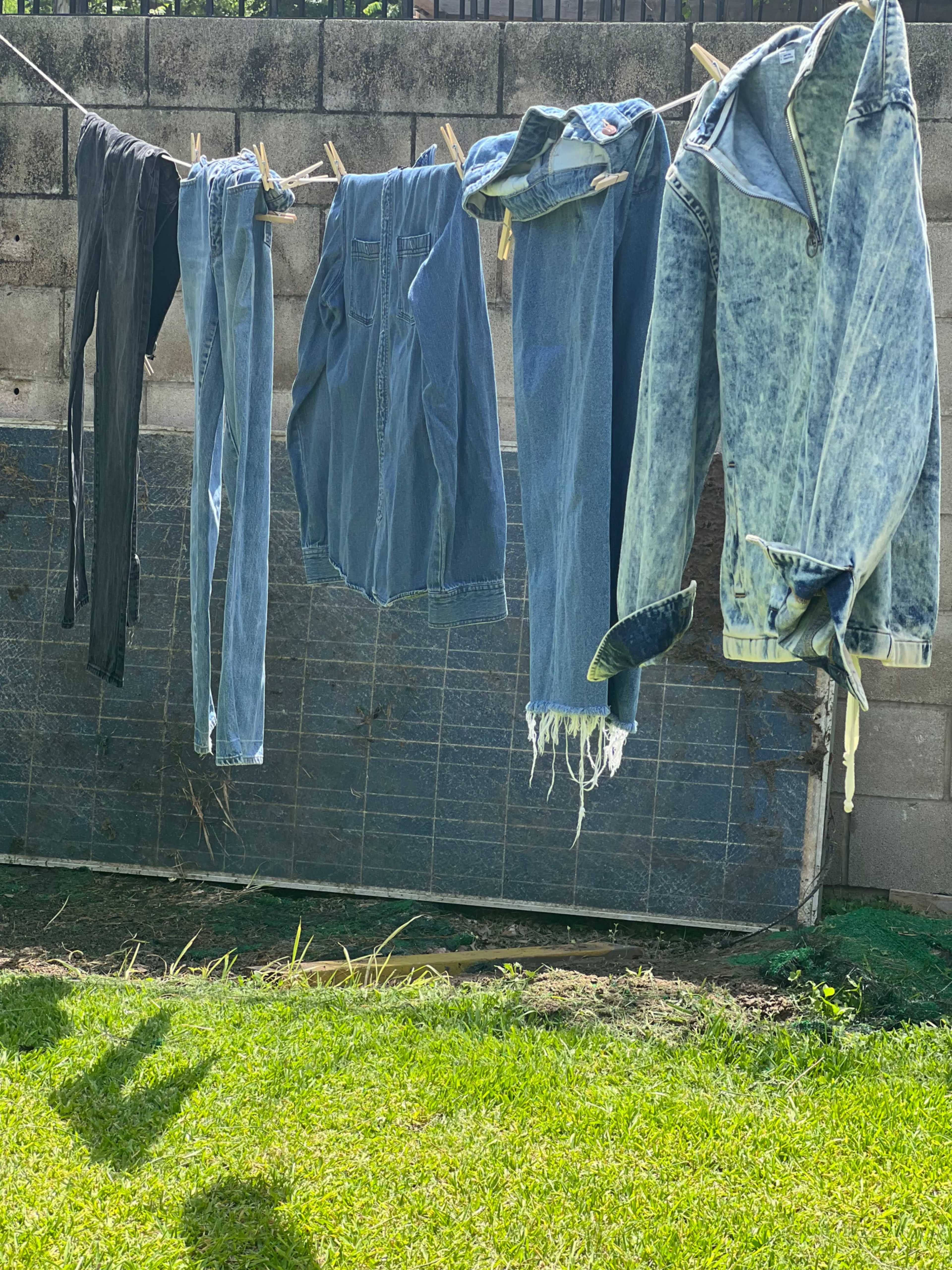 Clothes of various denim shades hang on a clothesline against a concrete wall.
