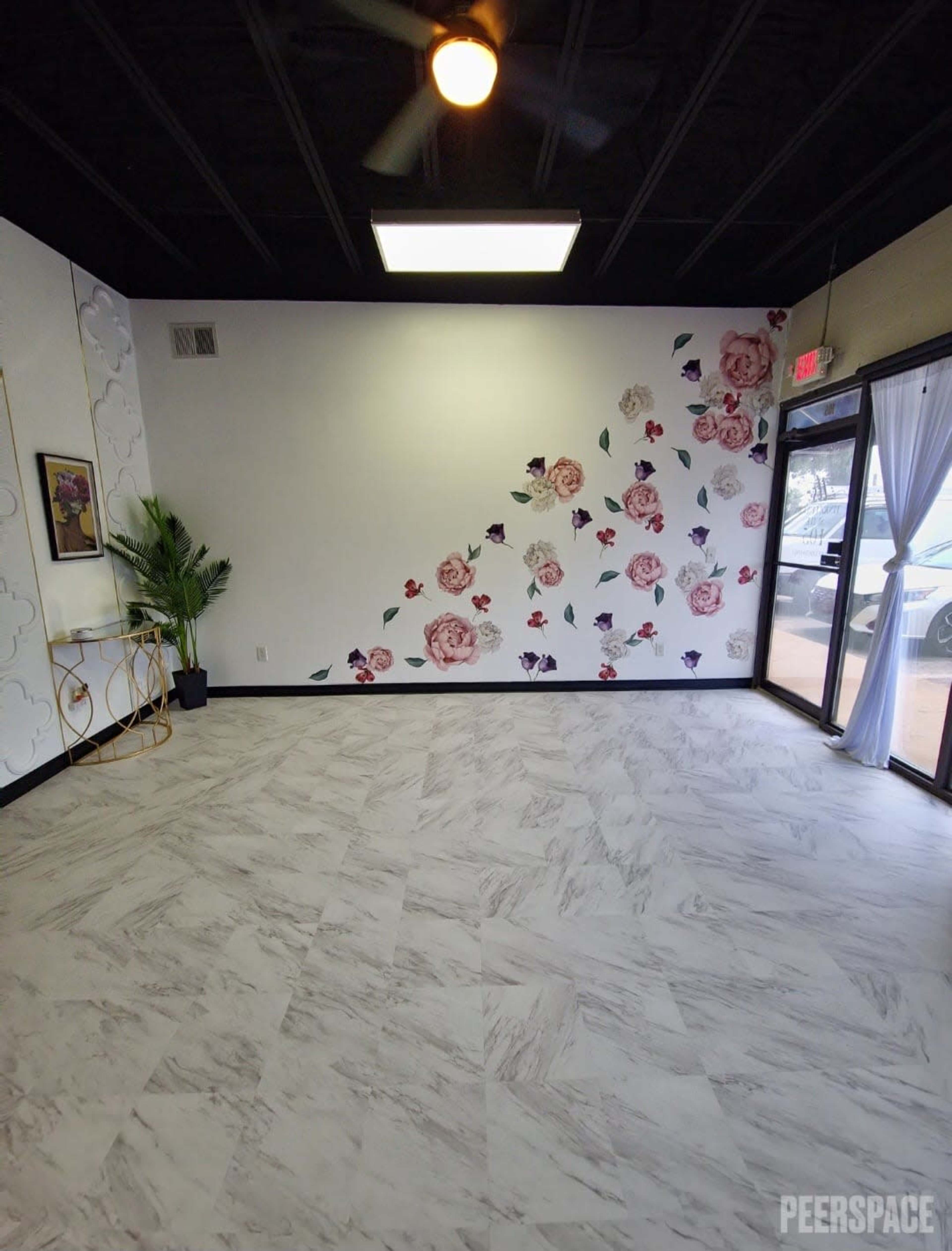 An empty room with a floral accent wall, large windows, and modern flooring.