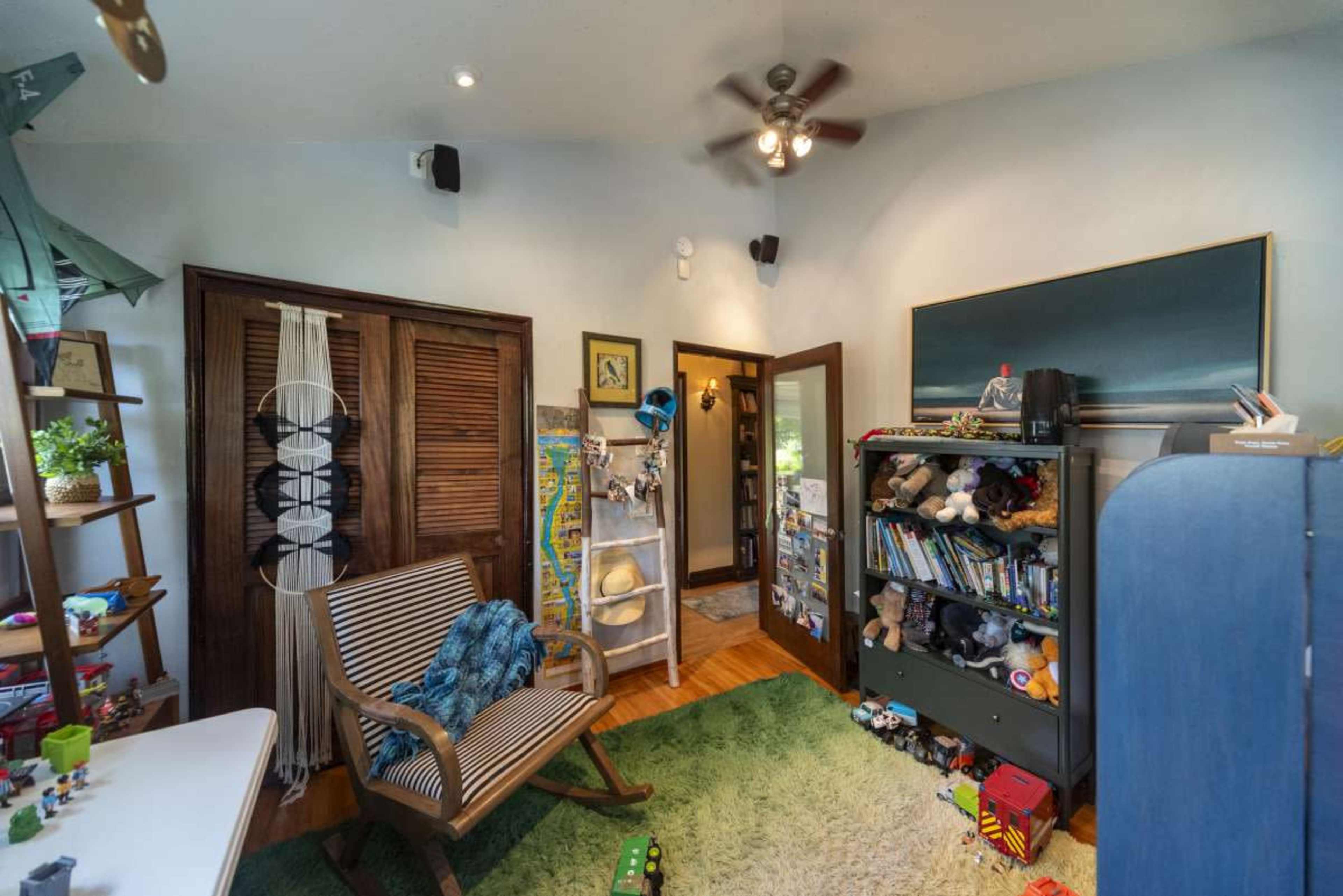 The image shows a children's room featuring a rocking chair, shelves filled with toys, and a doorway leading to another part of the house.