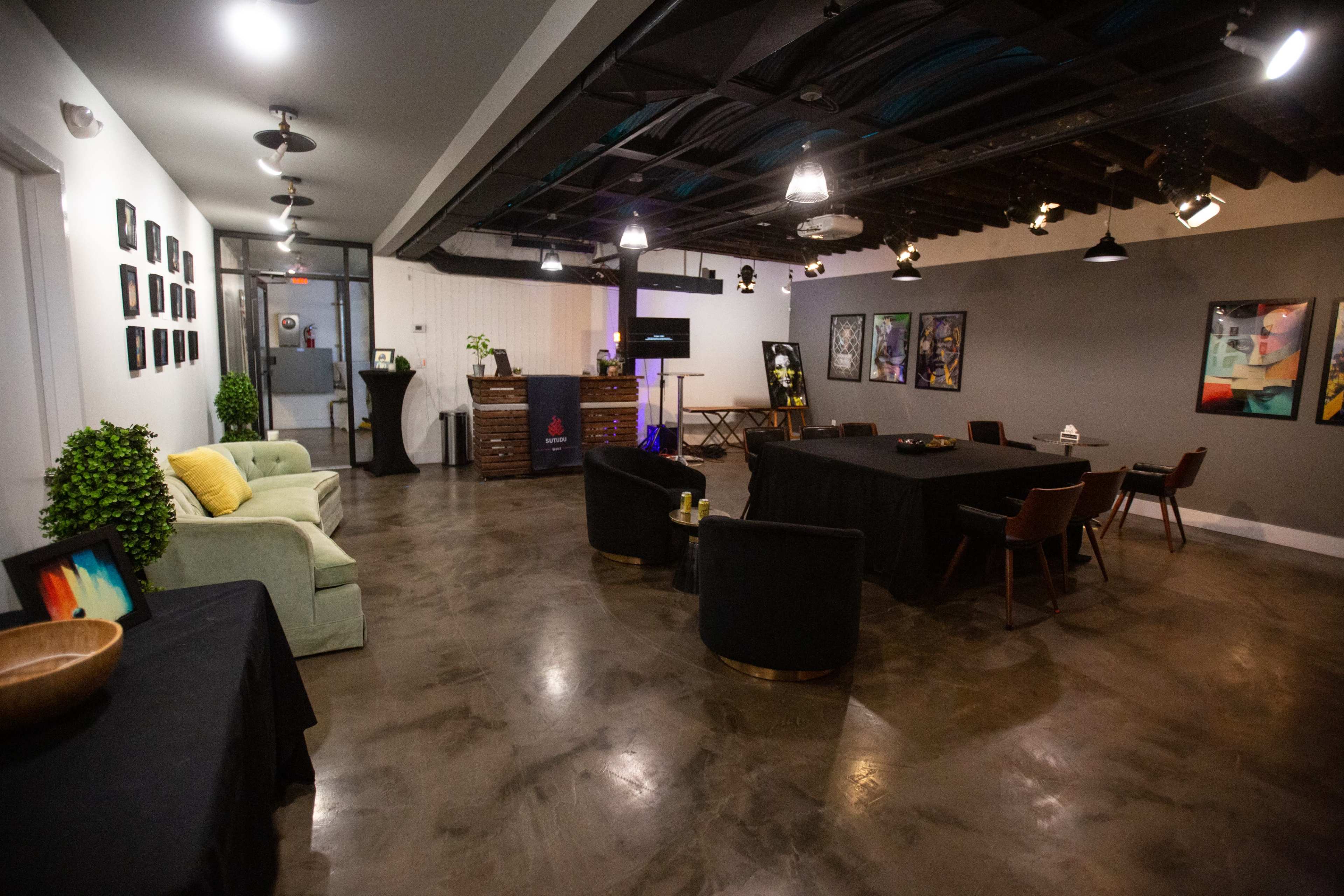 A modern multifunctional room with seating areas, a central table setup, and artwork displayed on the walls.