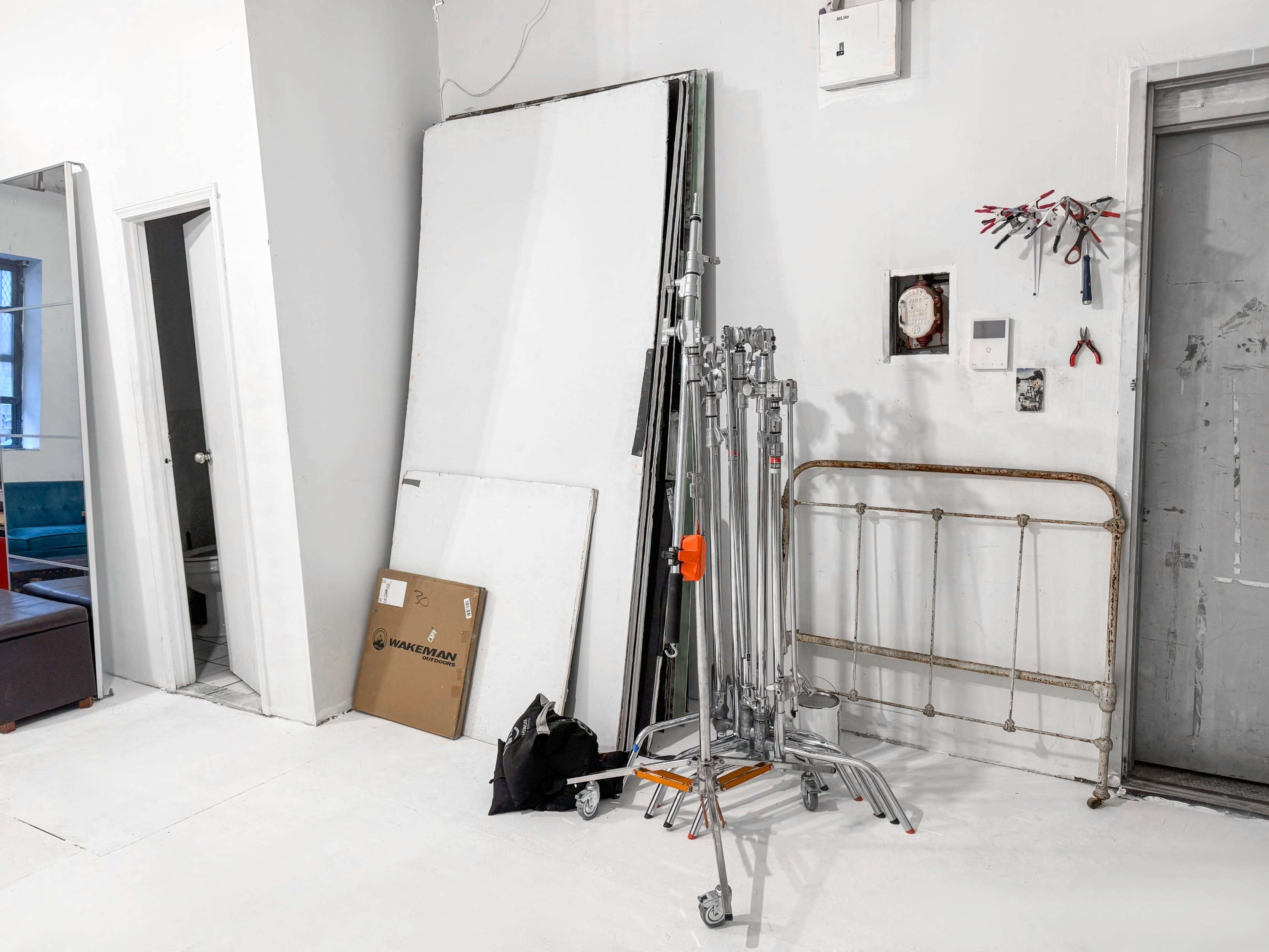 The image shows a corner of a room featuring stacked panels, a folding bed frame, and a wheeled cart with metal stands.