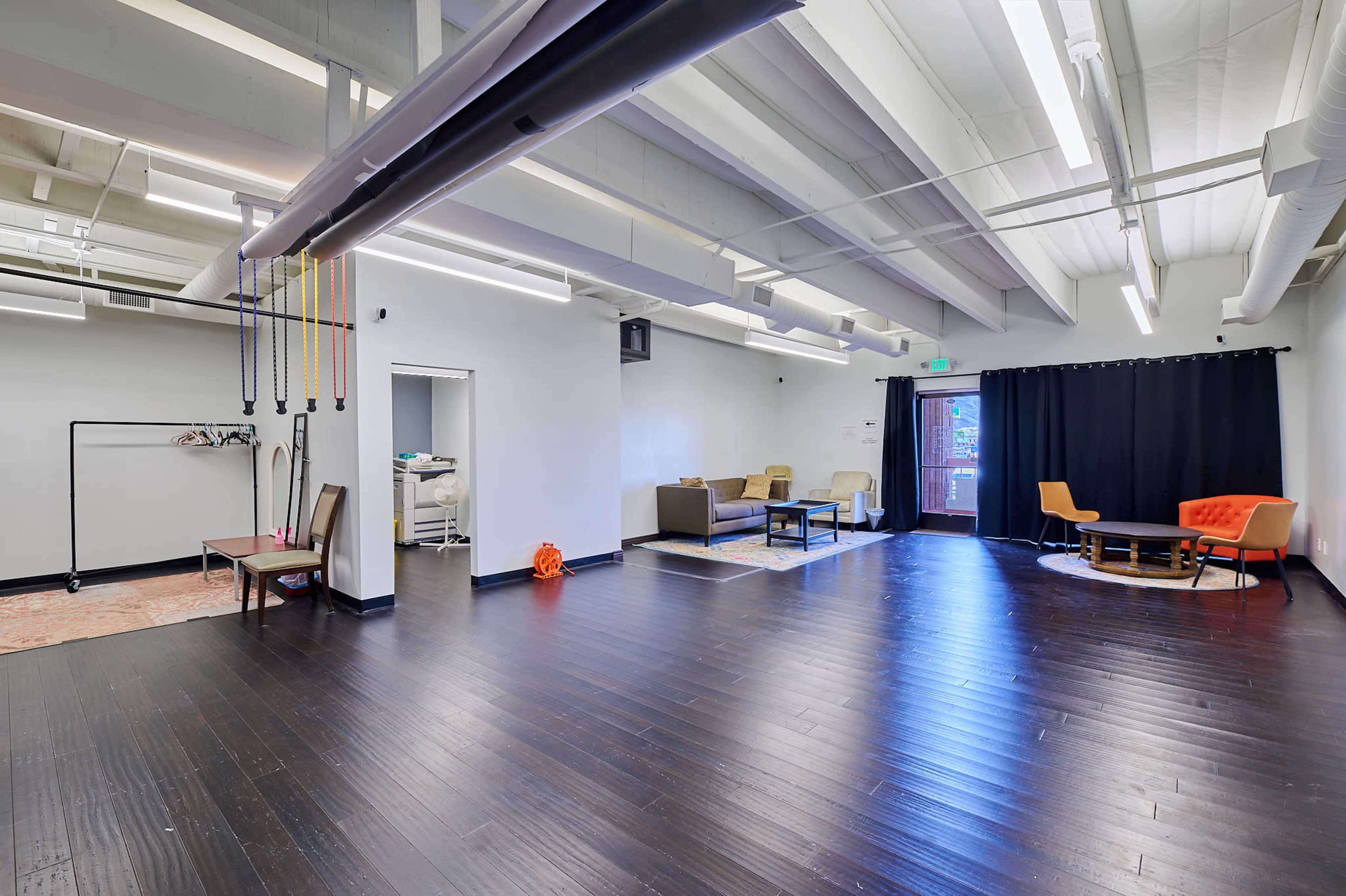 The image shows a spacious and well-lit room featuring a seating area with couches, an orange chair, and an exercise station with equipment.