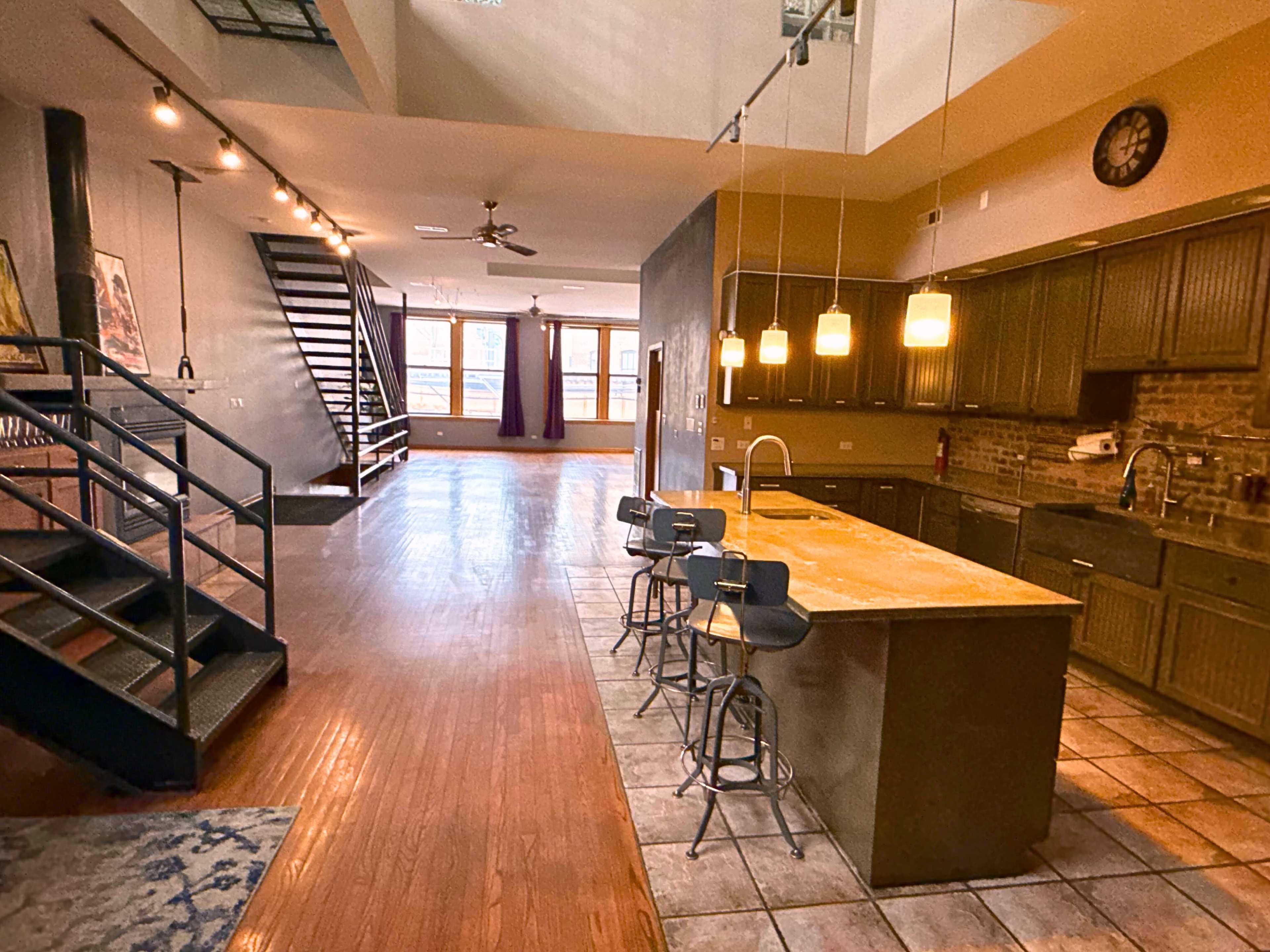 The image shows an open-concept living space with a kitchen island and a staircase leading to an upper level.
