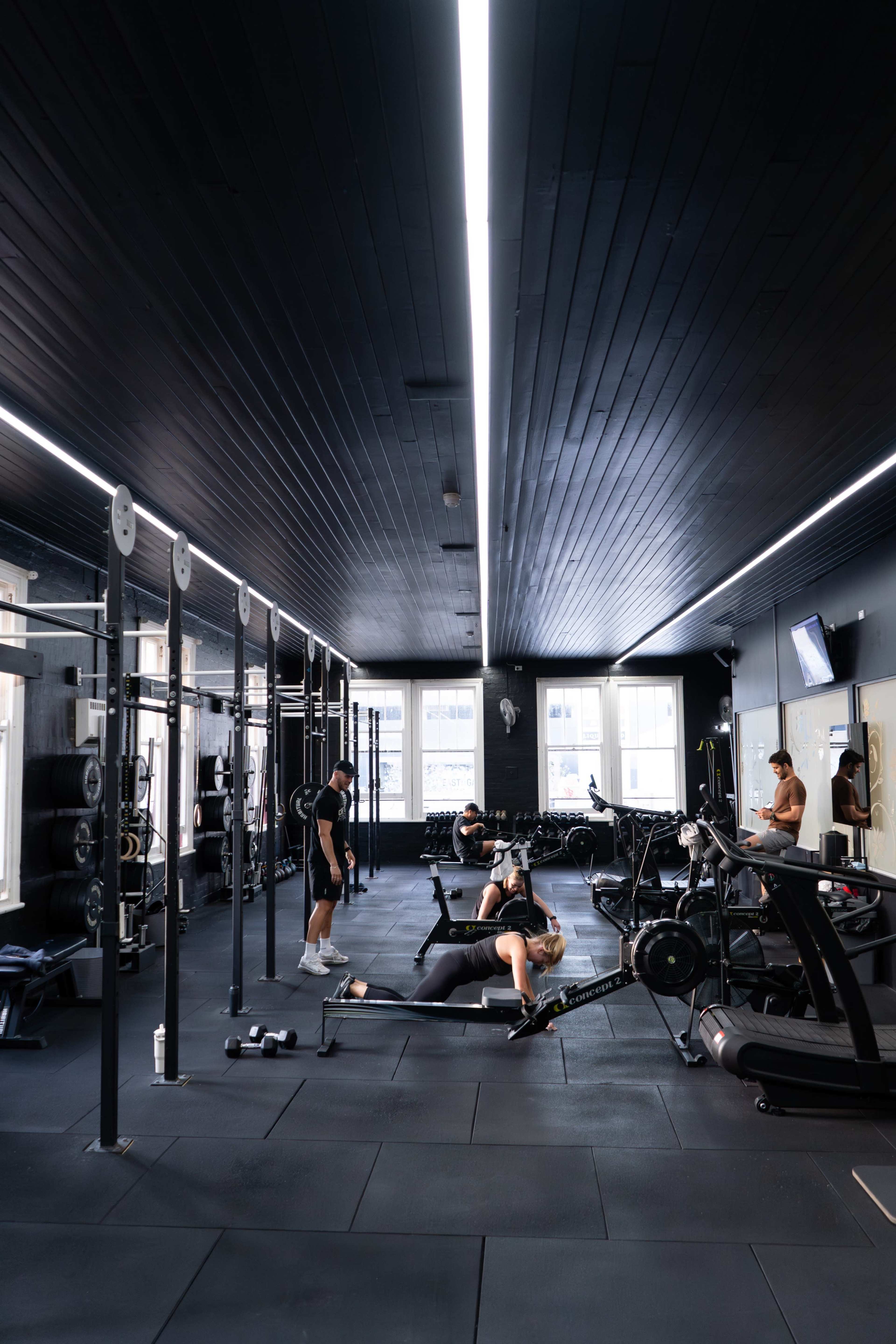 The image shows a spacious gym with several fitness machines and equipment, where multiple people are engaged in various workouts.